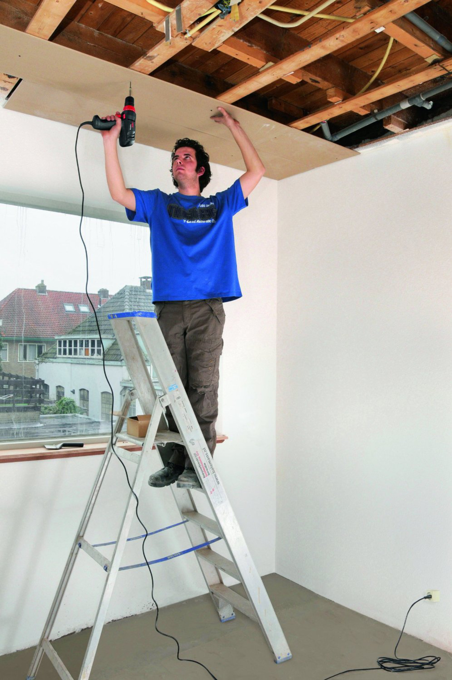Un uomo su una scala avvita un pannello in cartongesso al soffitto.