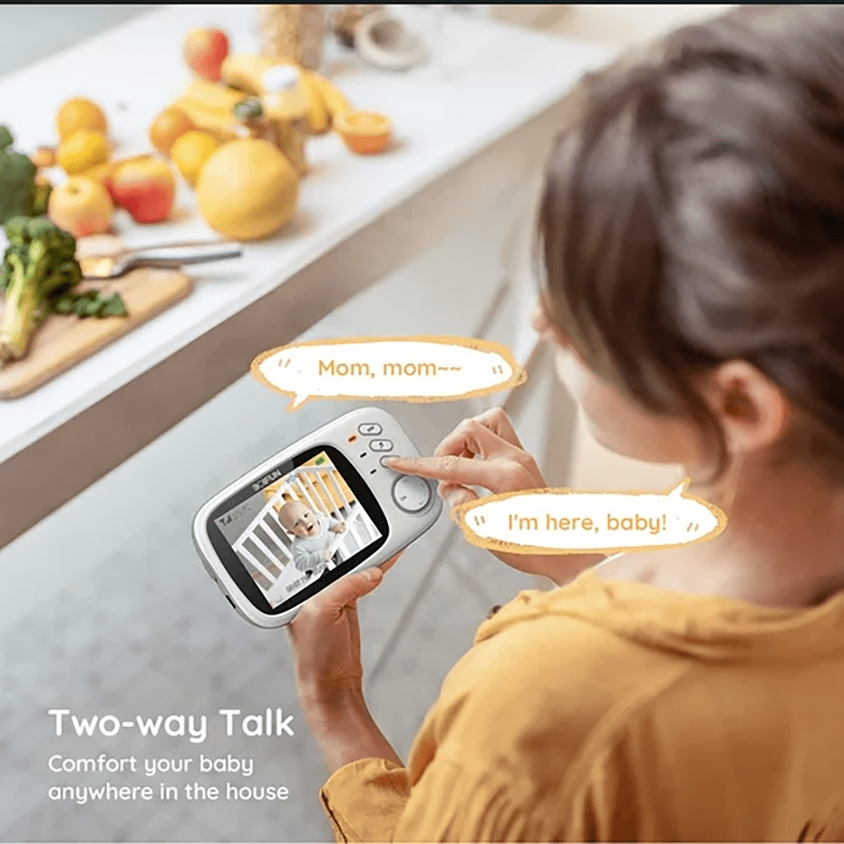 Eine Mutter benutzt ein Babyphone in der Küche, während Obst auf der Theke liegt.