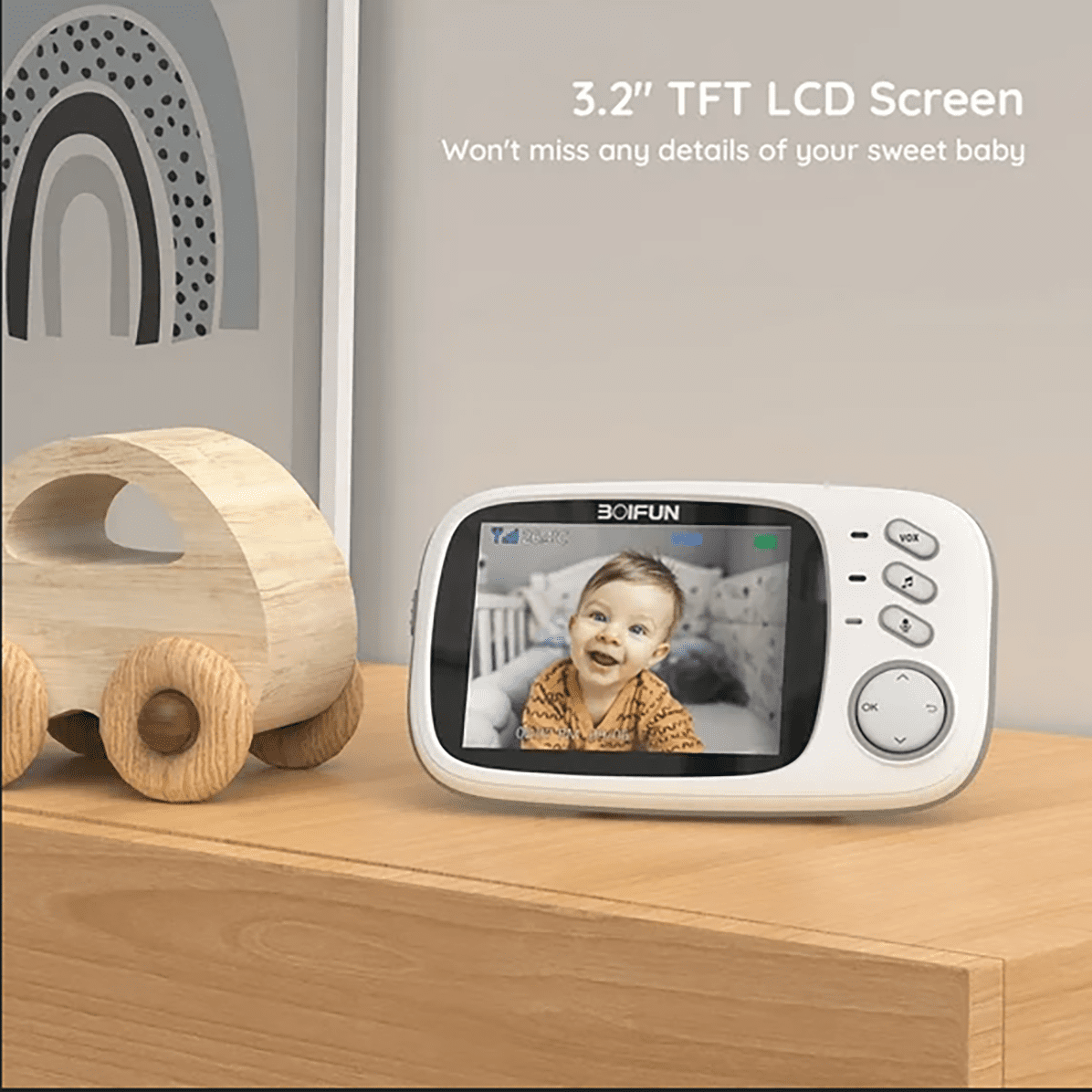 Ein Babyphone auf einer Holzkommode zeigt ein lächelndes Baby auf dem Bildschirm. Daneben ein hölzernes Spielzeugauto.