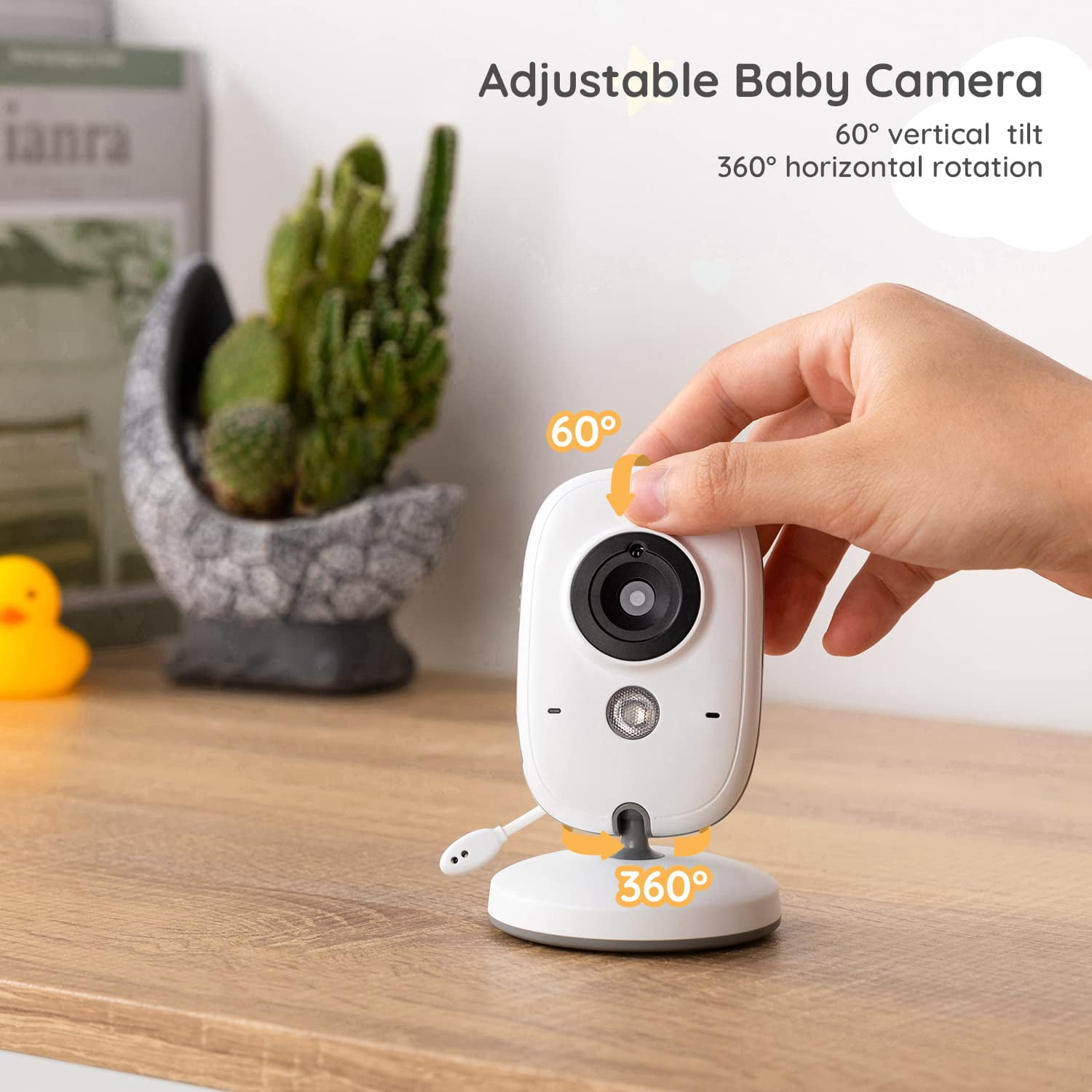 Hand berührt weiße Babykamera mit 60° Neigung und 360° Drehung auf Holztisch neben Kaktus.