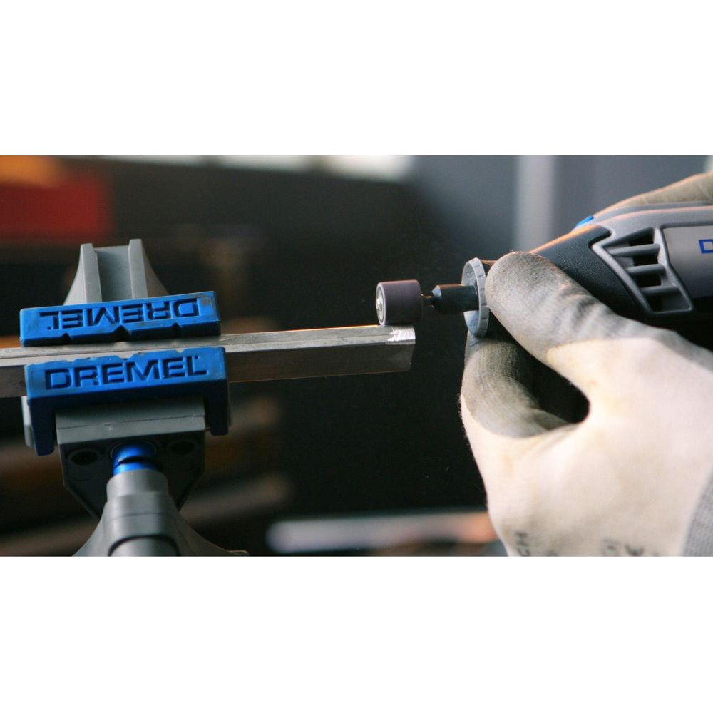 Eine von Handschuhen geschützte Hand nutzt ein Dremel-Werkzeug zum Schleifen eines Metallstabs in einem blauen Schraubstock.