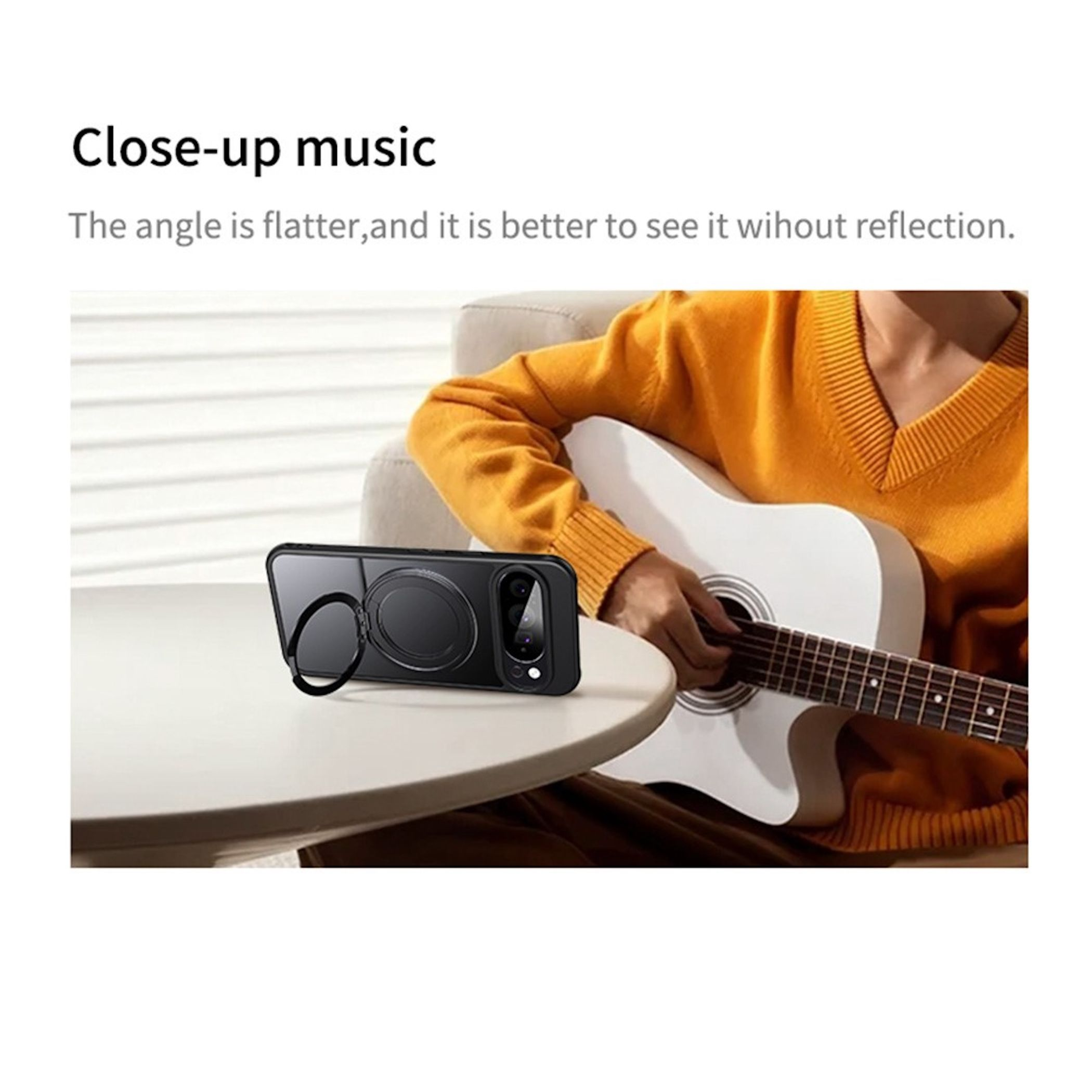 Eine Person im orangen Pullover spielt Gitarre, während ein Smartphone auf einem Tisch liegt.