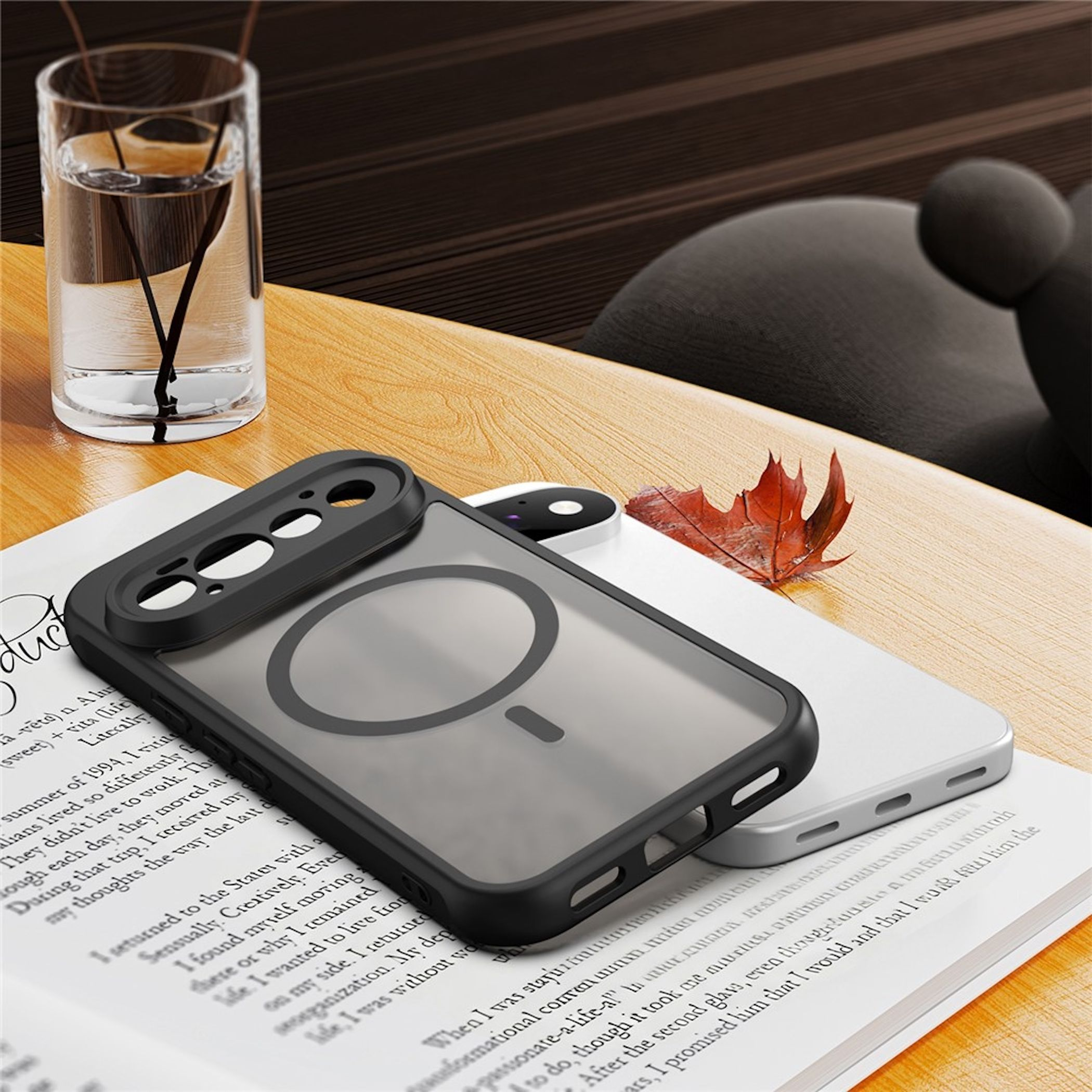 Eine schwarze Smartphone-Hülle liegt auf einem Buch, neben einem Glas Wasser und einem roten Blatt.