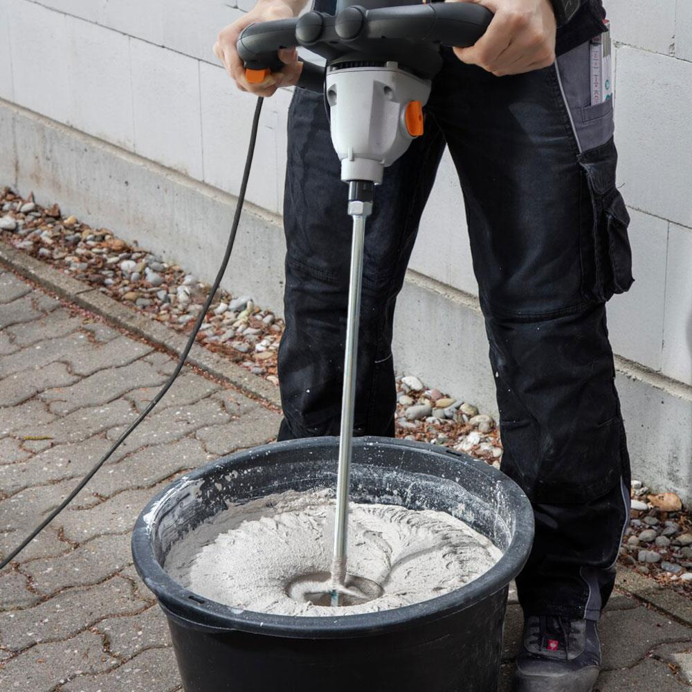Bir işçi, siyah bir kovada harç karıştırmak için elektrikli el mikseri kullanıyor.