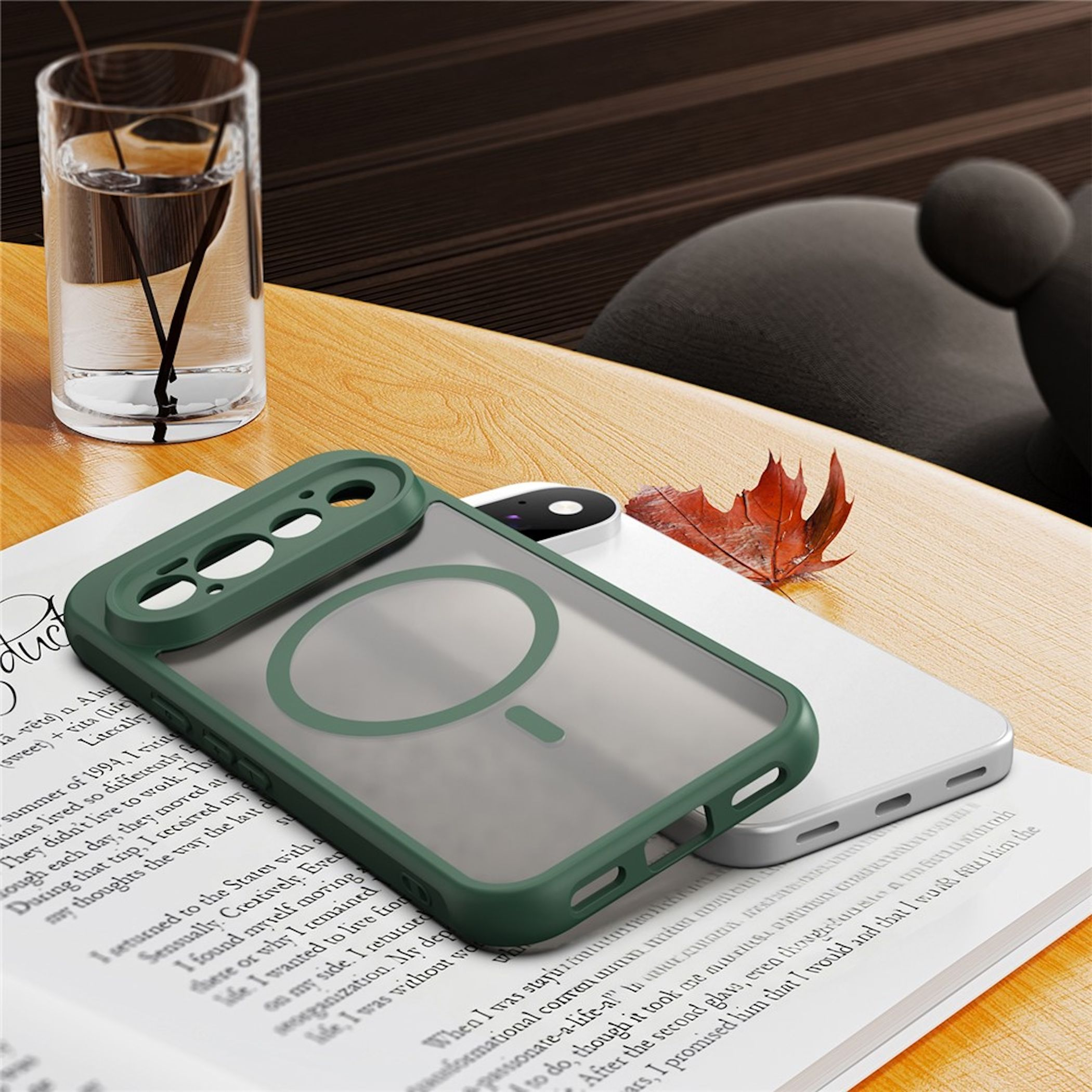 Eine grüne Smartphone-Hülle liegt auf einem Buch auf einem Holztisch, daneben ein Glas Wasser.