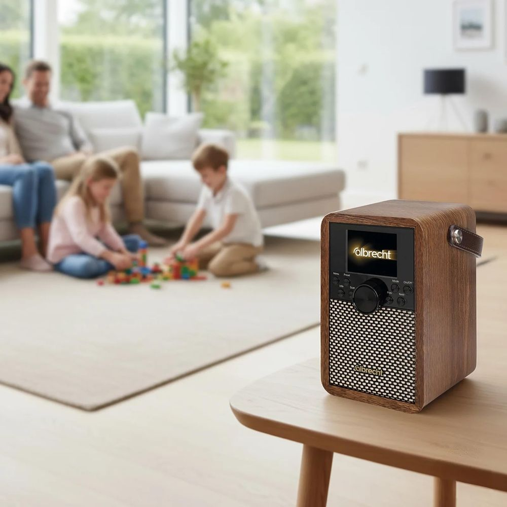 Ein hölzernes Albrecht-Radio steht auf einem Tisch in einem hellen Wohnzimmer, während eine Familie im Hintergrund spielt.