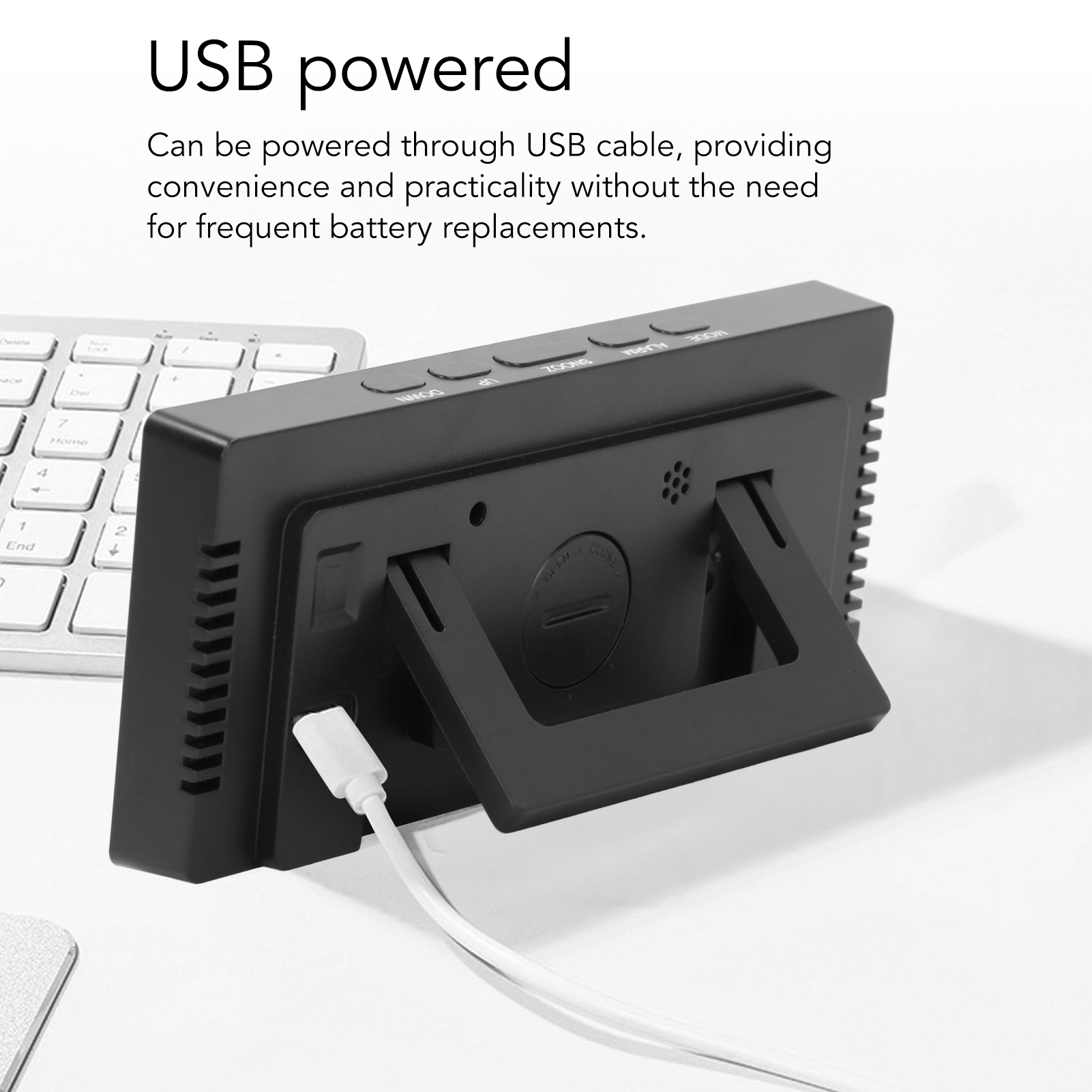 Ein schwarzer Digitalwecker mit USB-Kabel steht auf einem Tisch neben einer Tastatur.