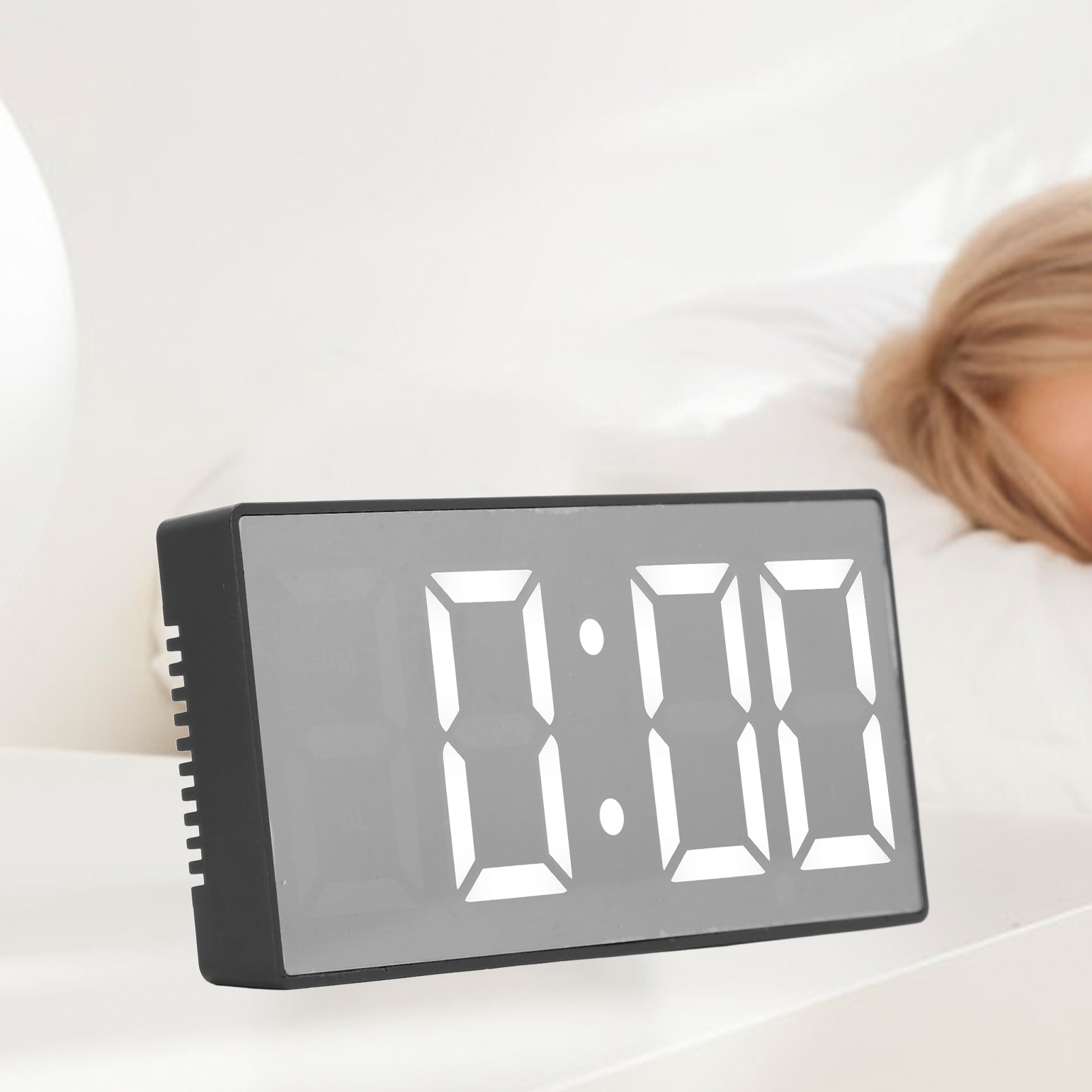 Ein moderner schwarzer Digitalwecker mit hellen weißen Ziffern zeigt 0:00 auf einem Nachttisch.