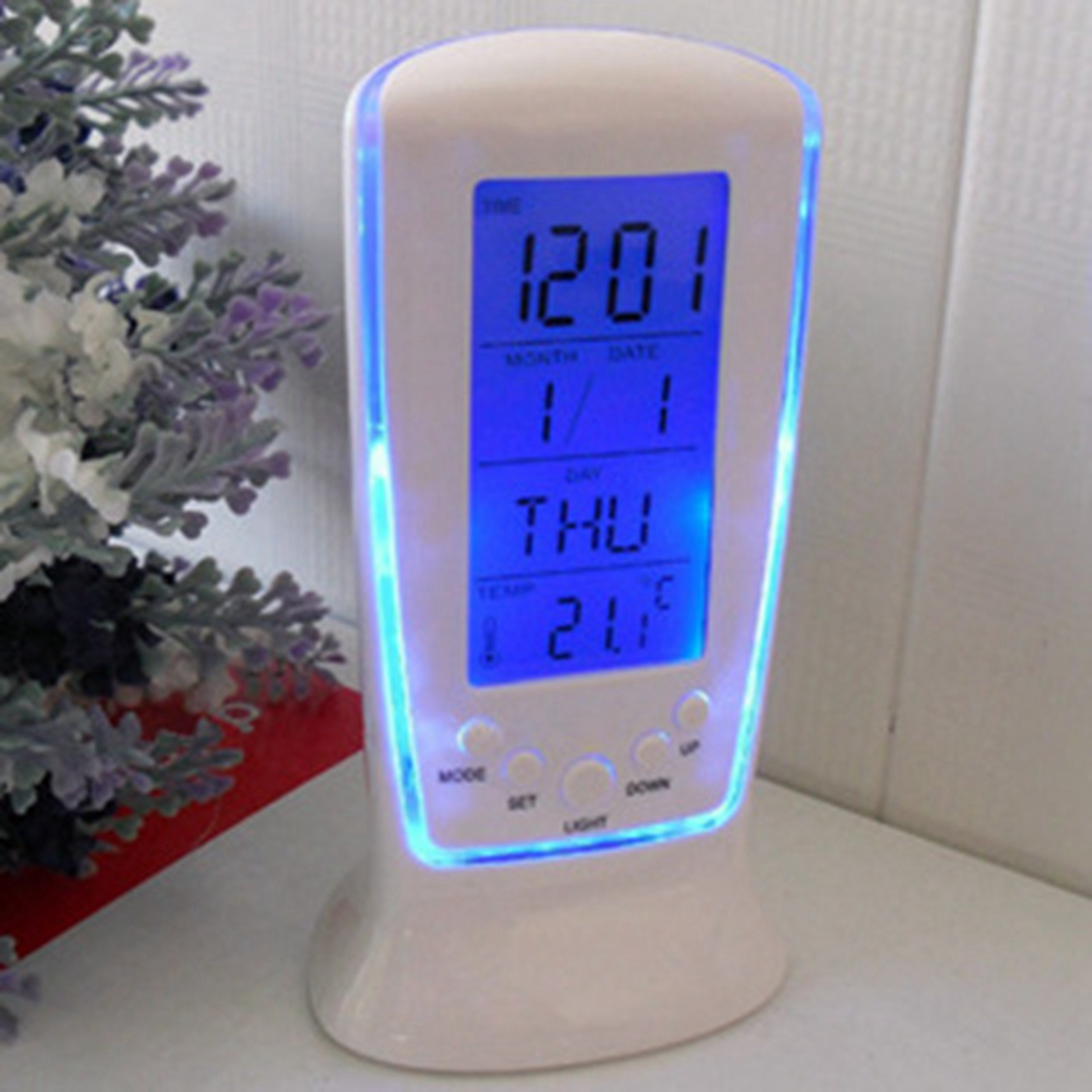 Eine weiße digitale Uhr mit blauer Hintergrundbeleuchtung und Display für Uhrzeit, Datum und Temperatur steht auf einem Tisch.