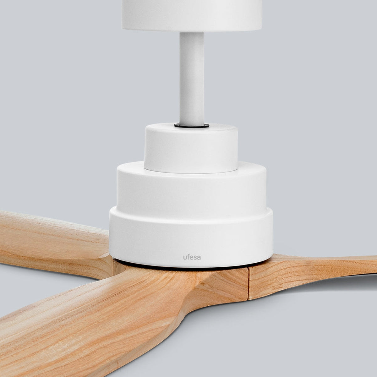 Un ventilador de techo blanco con tres aspas de madera y carcasa cilíndrica sobre fondo gris.