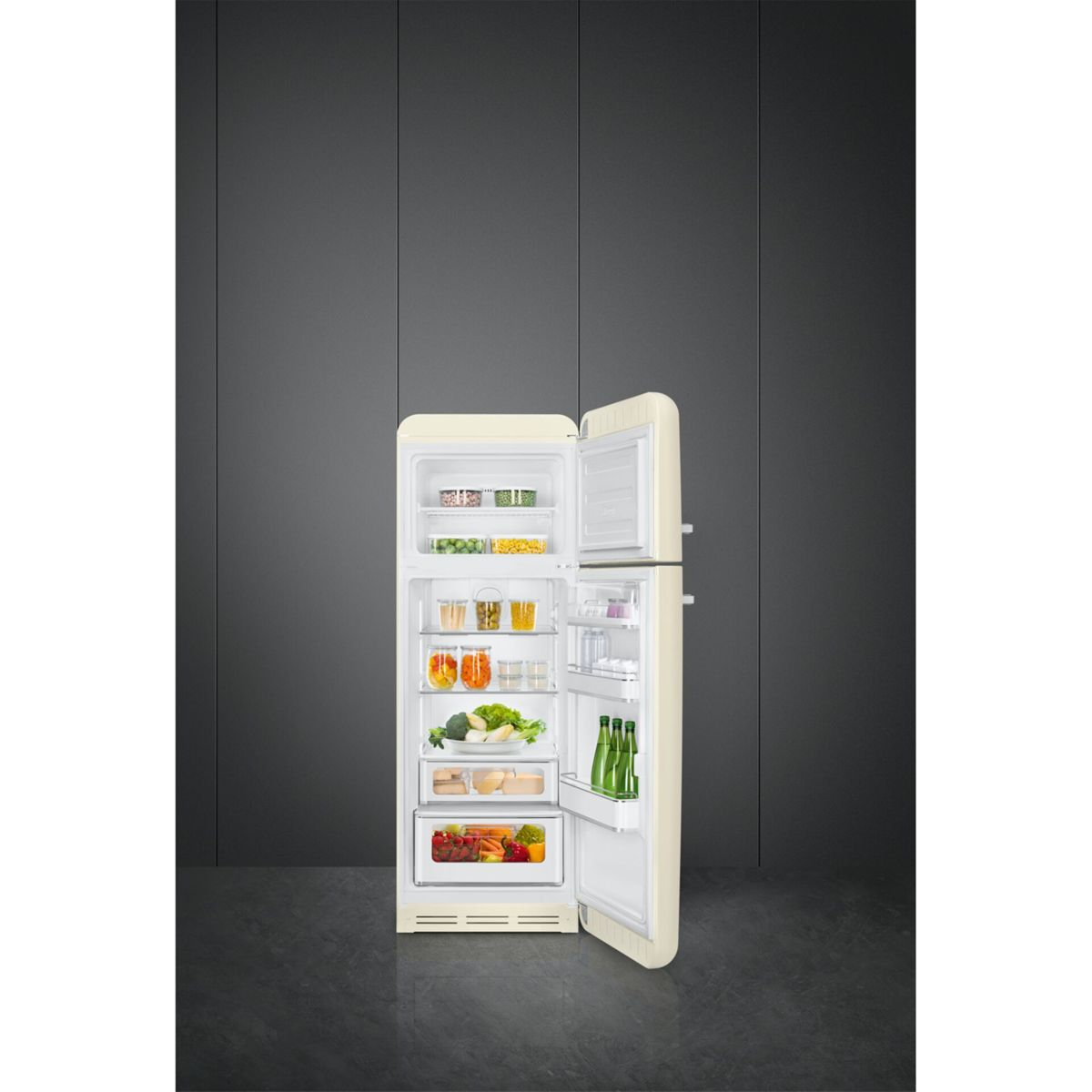 Un refrigerador retro abierto de color crema lleno de comida, contra una pared gris oscura.