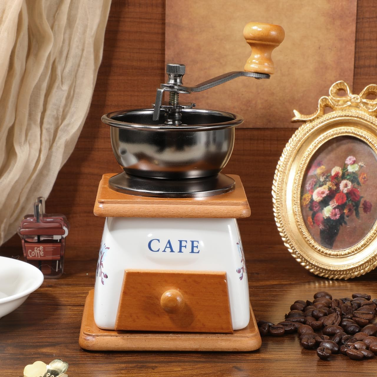 Eine manuelle Kaffeemühle mit weißem Keramikkörper und Holz auf einem Holztisch, umgeben von Kaffeebohnen.