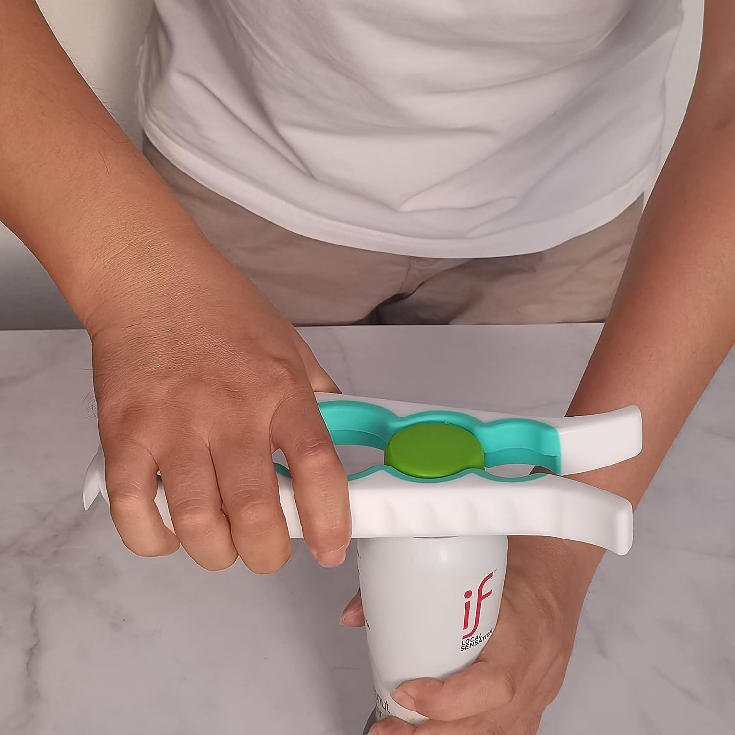 Person öffnet eine weiße Dose mit einem weißen und grünen Werkzeug am Tisch.