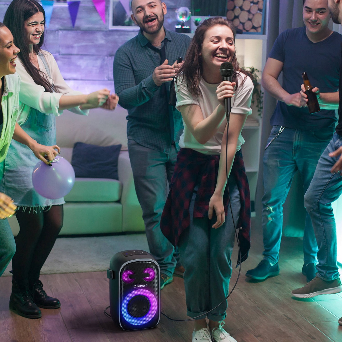 Freunde machen eine Karaoke-Party zu Hause, eine Frau singt in ein Mikrofon neben einem leuchtenden Lautsprecher.