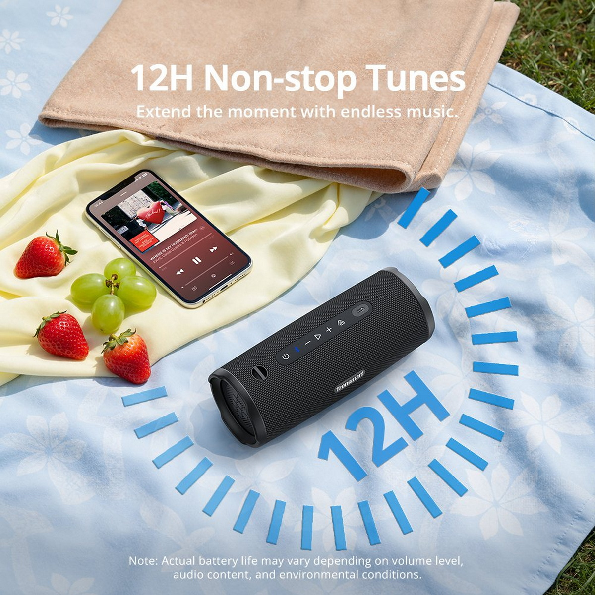 Tronsmart-Lautsprecher, Smartphone, Erdbeeren und Trauben auf einer blauen Picknickdecke.