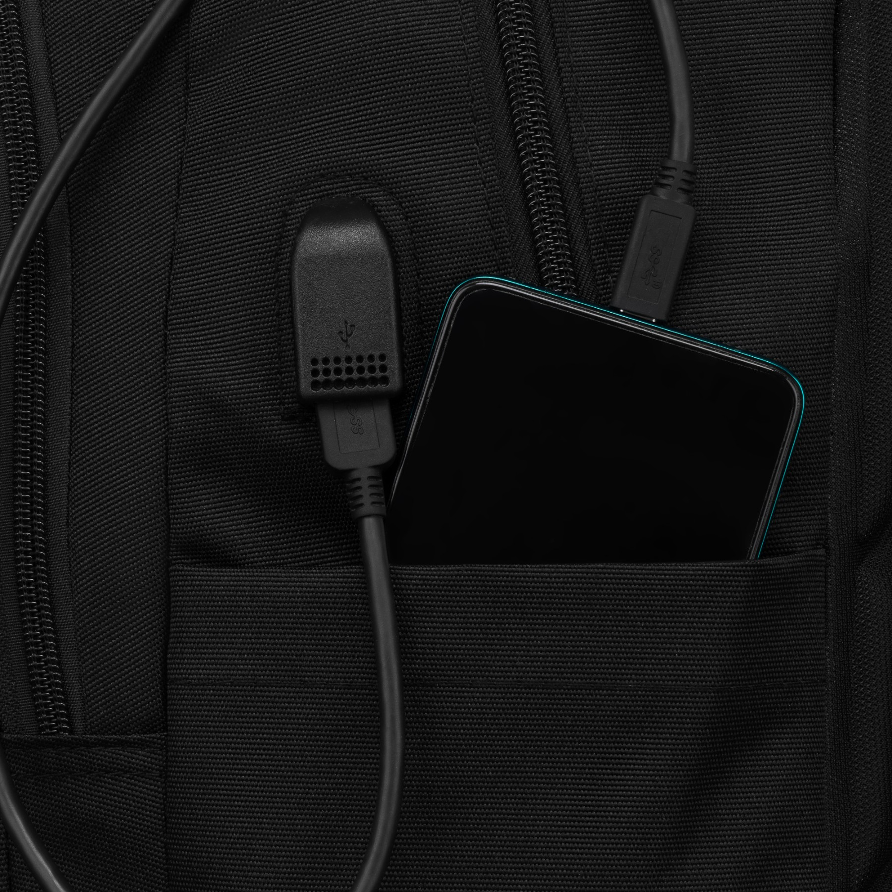 Smartfon i kable USB w zewnętrznej kieszeni czarnego plecaka.
