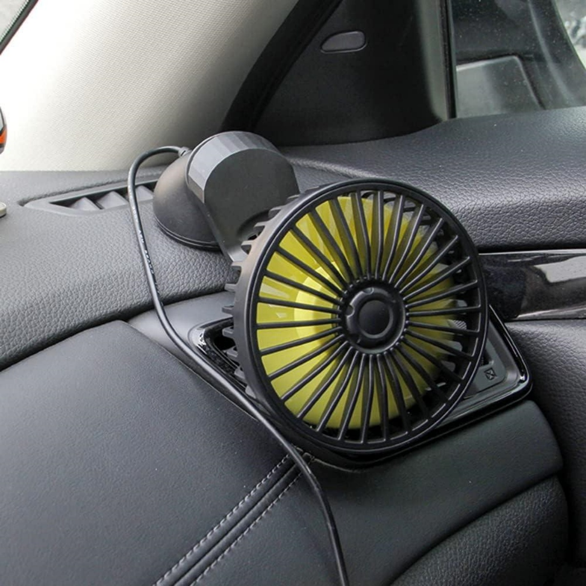 Ein kleiner schwarzer und gelber Autoventilator ist am Armaturenbrett in der Nähe des Fensters befestigt.