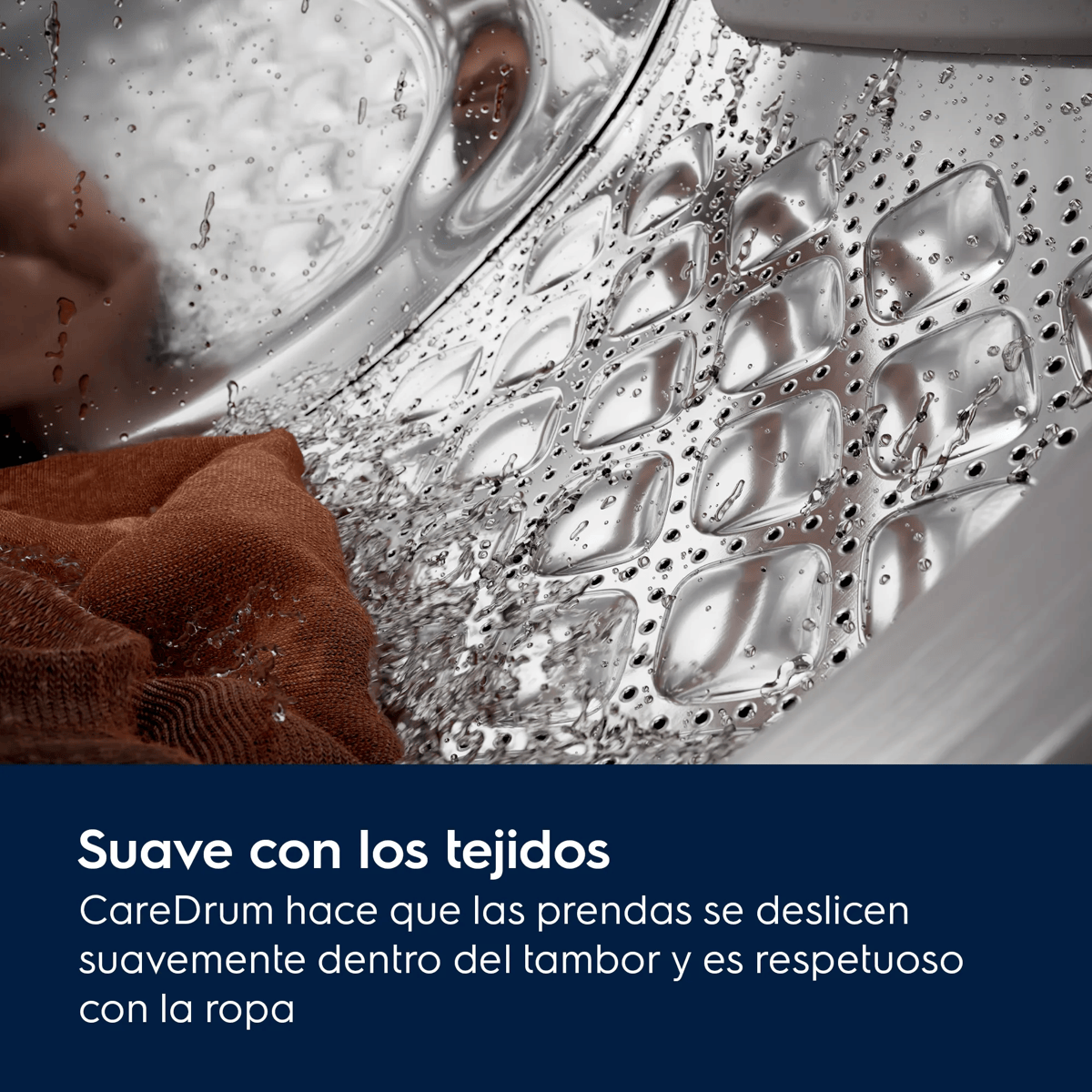 Primer plano del tambor de una lavadora de acero inoxidable con patrones en relieve, gotas de agua y una prenda marrón.
