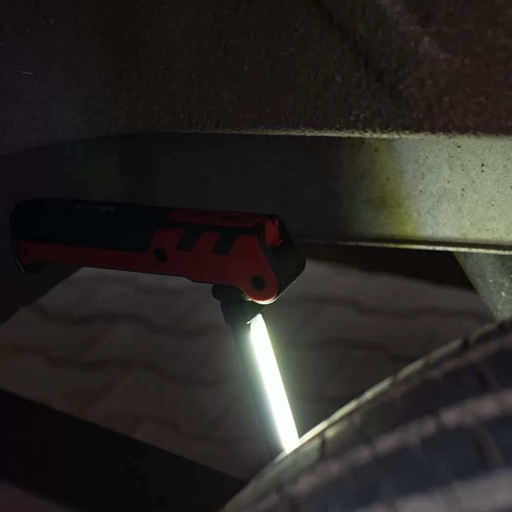 Czerwono-czarna lampa robocza oświetla podwozie i oponę pojazdu w ciemności.