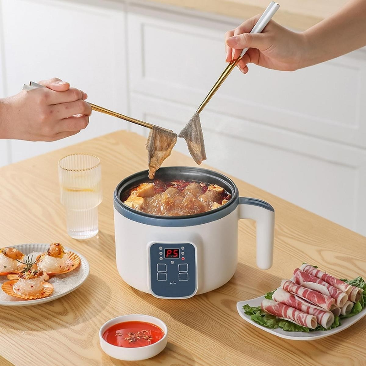 Zwei Personen nutzen Stäbchen, um Essen in einen kleinen Elektro-Hot-Pot auf einem Holztisch mit Fleisch und Meeresfrüchten zu tauchen.