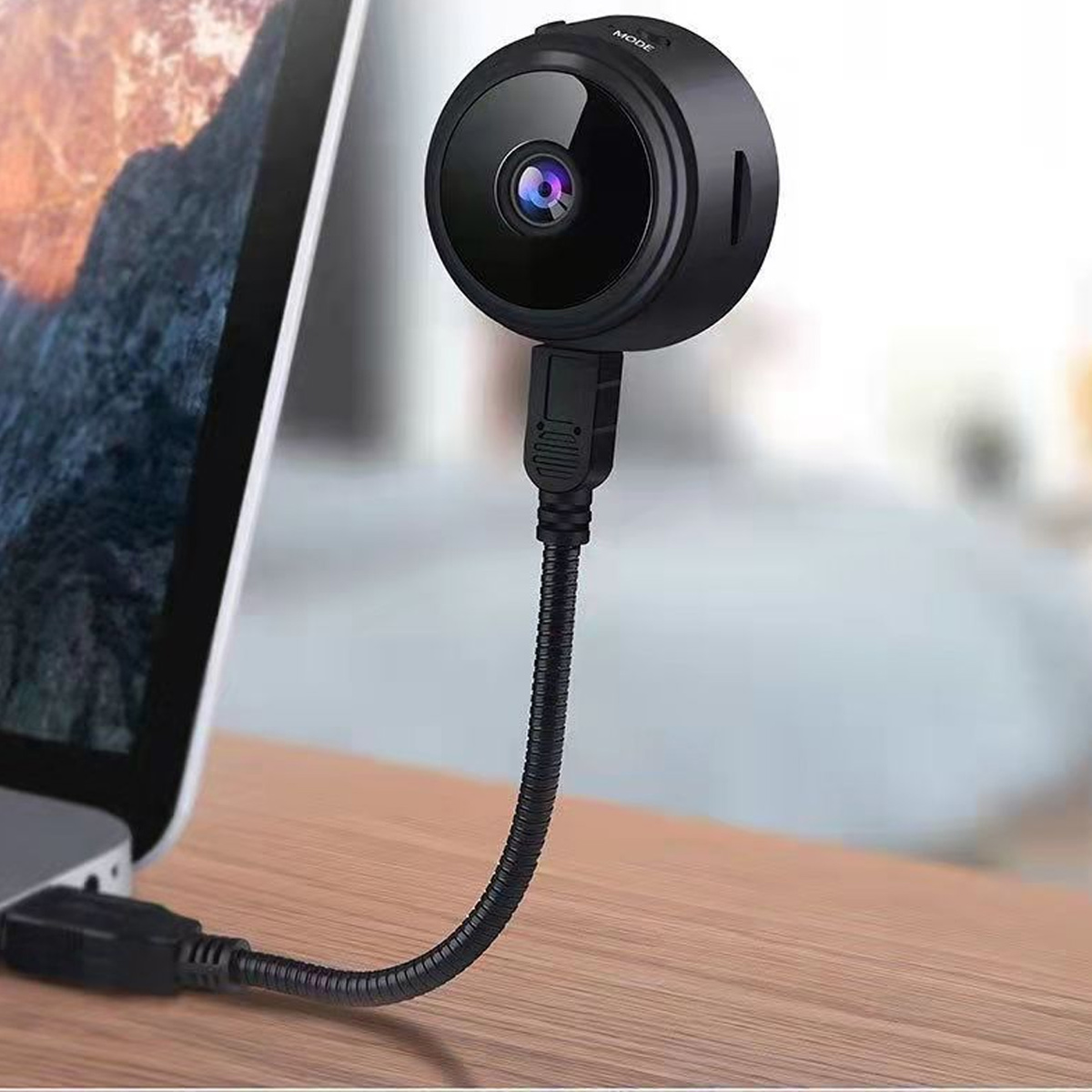 Eine kleine schwarze Mini-Kamera ist über ein USB-Kabel mit einem Laptop auf einem Holztisch verbunden.