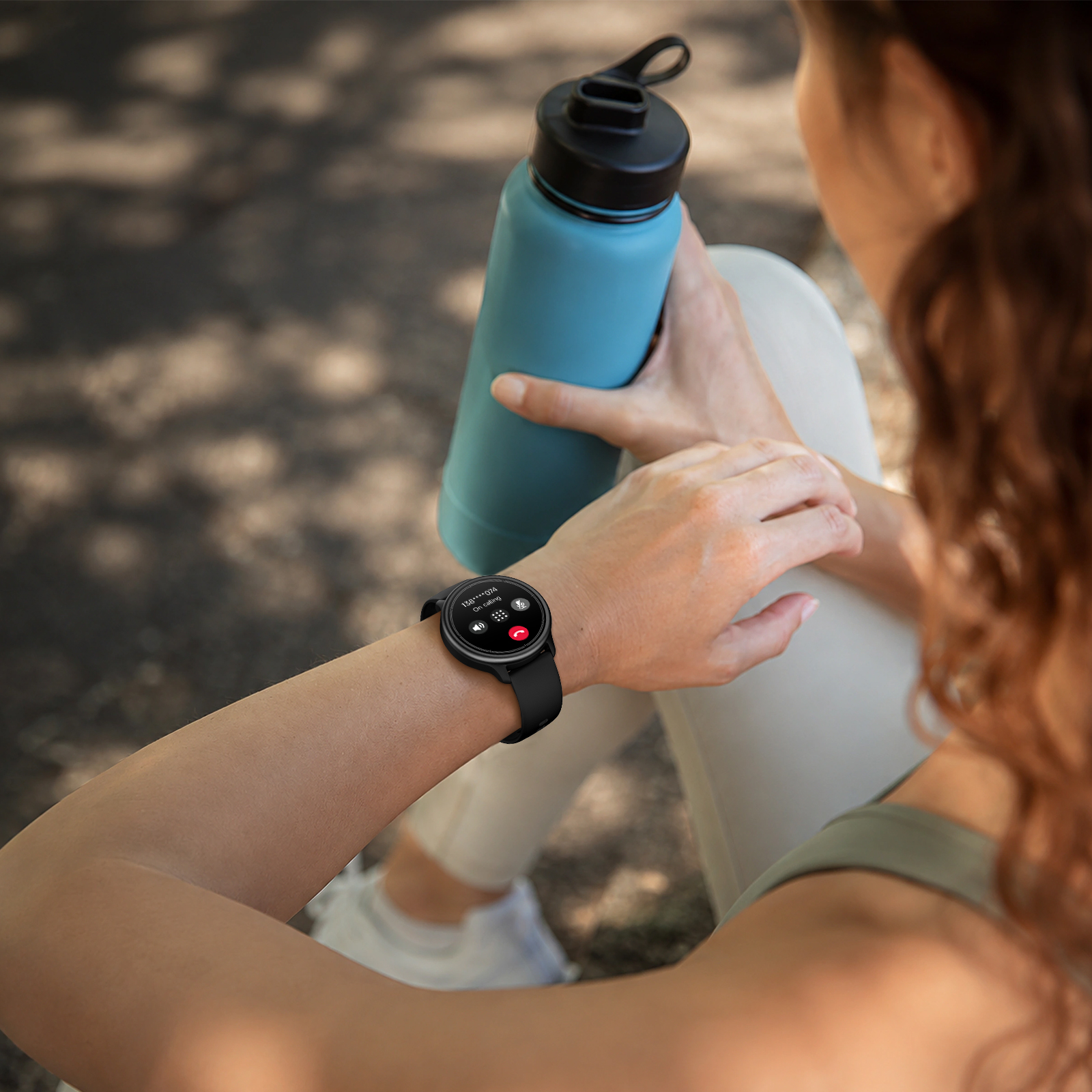 Una mujer sostiene una botella de agua azul mientras mira un reloj inteligente con una llamada entrante.