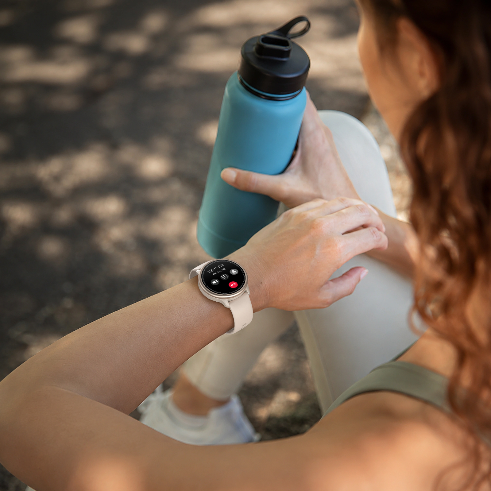 Mujer en ropa deportiva sosteniendo una botella de agua azul y mirando su reloj inteligente.