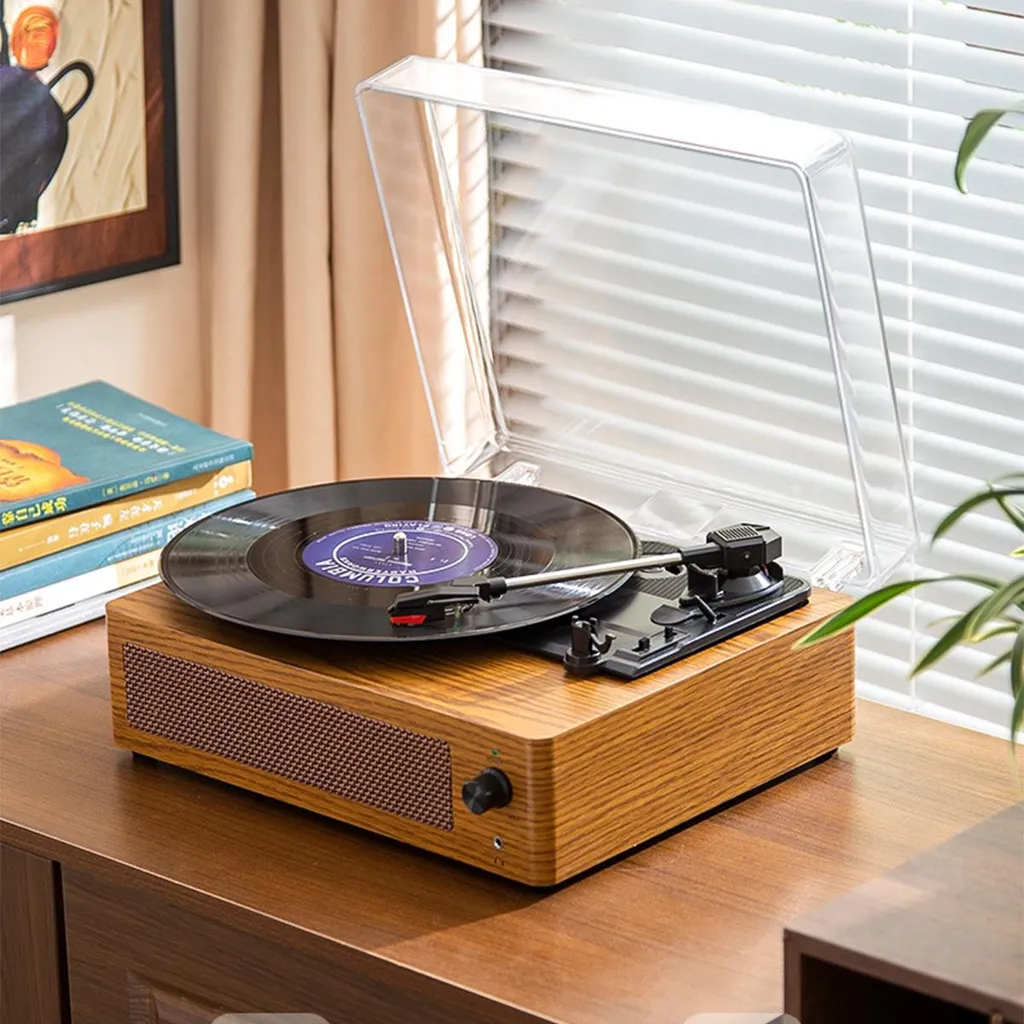 Ein Plattenspieler aus Holz mit schwarzer Vinylplatte, offener Klarsicht-Staubschutzhaube und Büchern auf einem Holztisch.