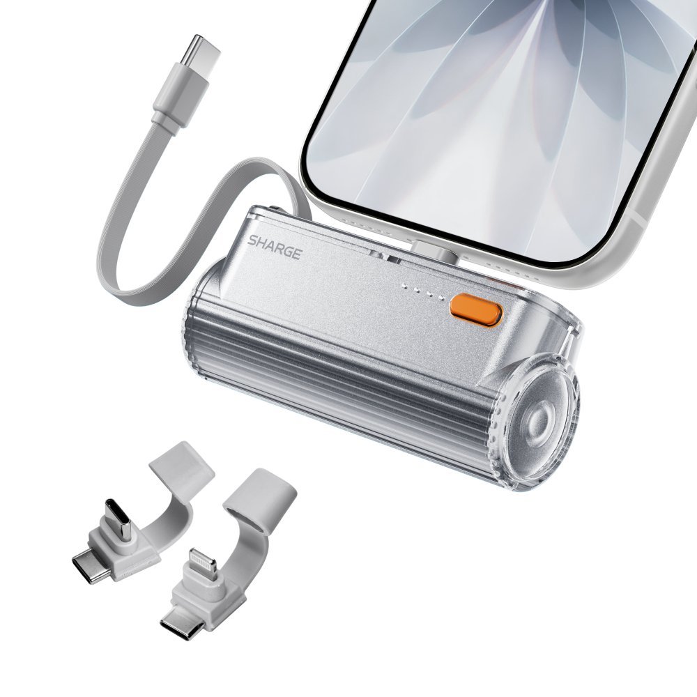 Silberne Sharge Powerbank mit integriertem Stecker lädt ein Smartphone. Zwei zusätzliche Adapter liegen daneben.