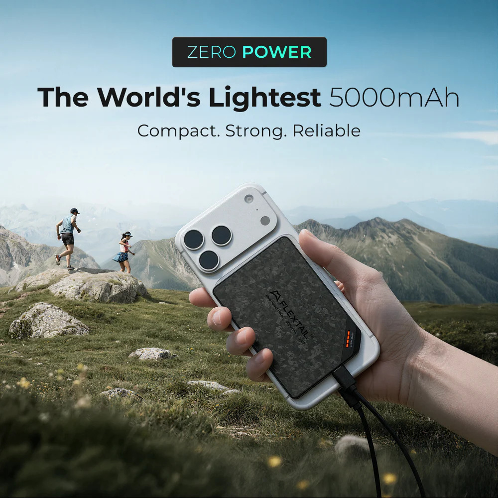 Hand hält eine Powerbank im Bergpanorama mit Läufern im Hintergrund.