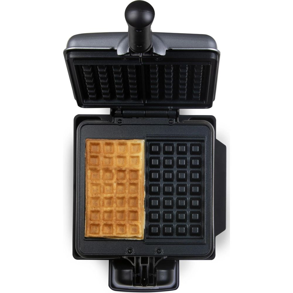 Ein offenes Waffeleisen mit einer halb fertigen goldenen Waffel und einer leeren Form auf weißem Hintergrund.