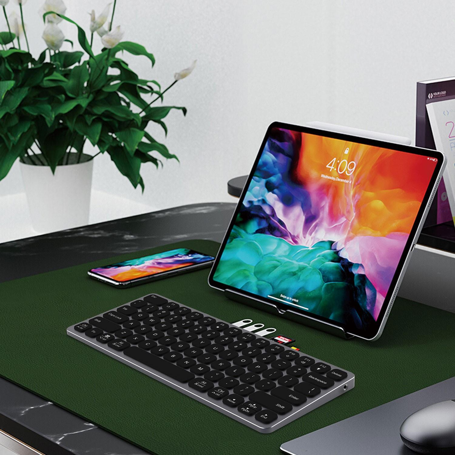 Standda bir tablet, kompakt bir klavye ve saksı bitkisinin yanındaki yeşil mat üzerinde bir akıllı telefon.