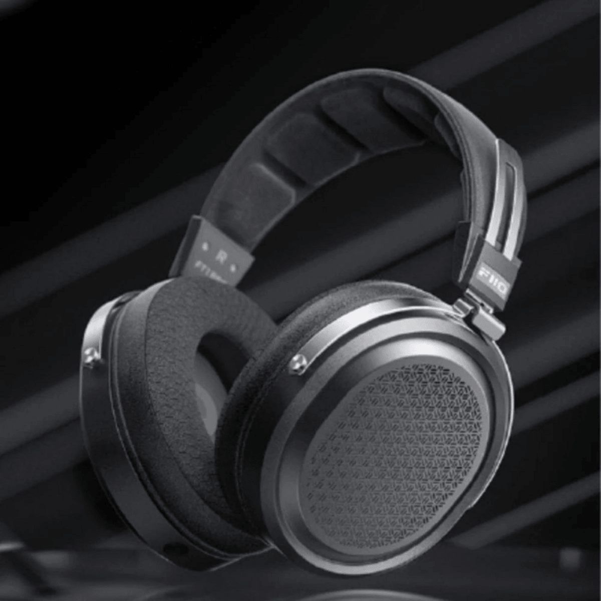 Auriculares supraurales negros con copas estampadas flotan sobre un fondo oscuro.