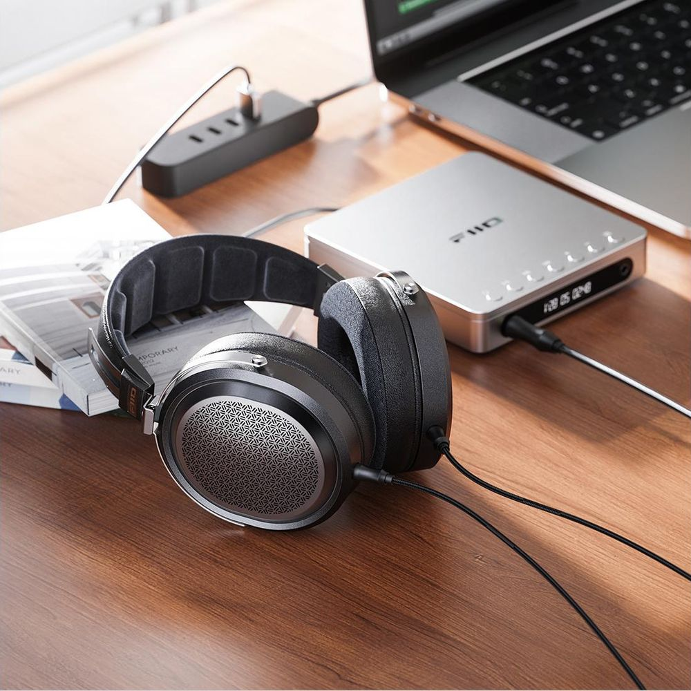 Auriculares supraaurales negros en un escritorio de madera junto a un DAC, portátil y libros.