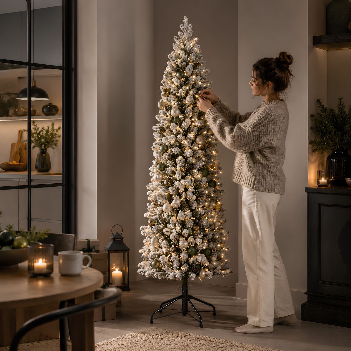 Een vrouw in een lichte trui versiert een grote, sneeuwbedekte kerstboom met lichtjes in een woonkamer.