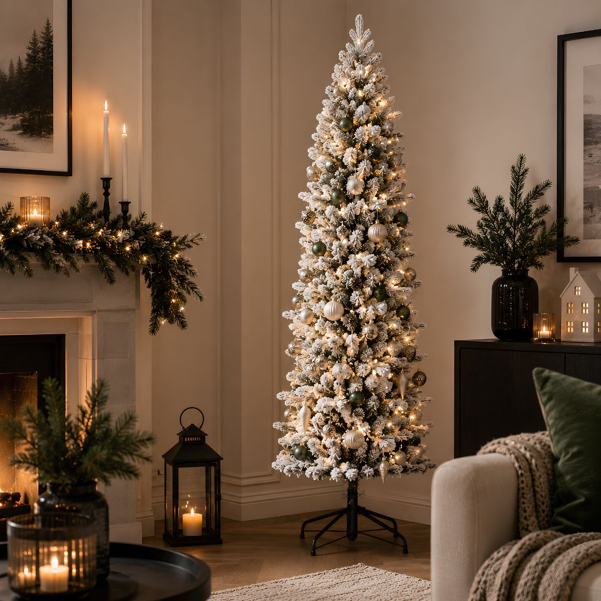 Een slanke, besneeuwde kerstboom met lichtjes en ornamenten in een warm verlichte woonkamer.