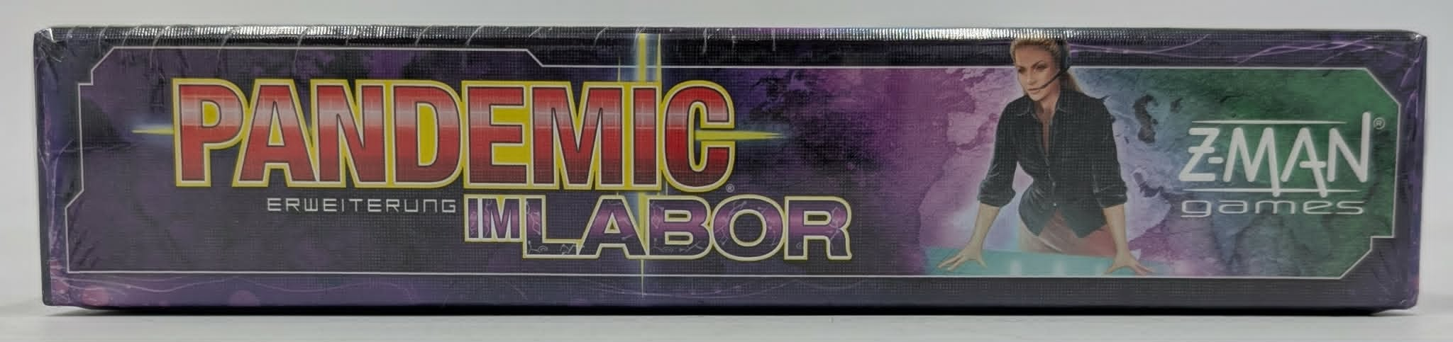 Seitenansicht der Brettspielbox "Pandemic: Im Labor" von Z-Man Games mit einer Frau mit Headset vor lila-grünem Hintergrund.