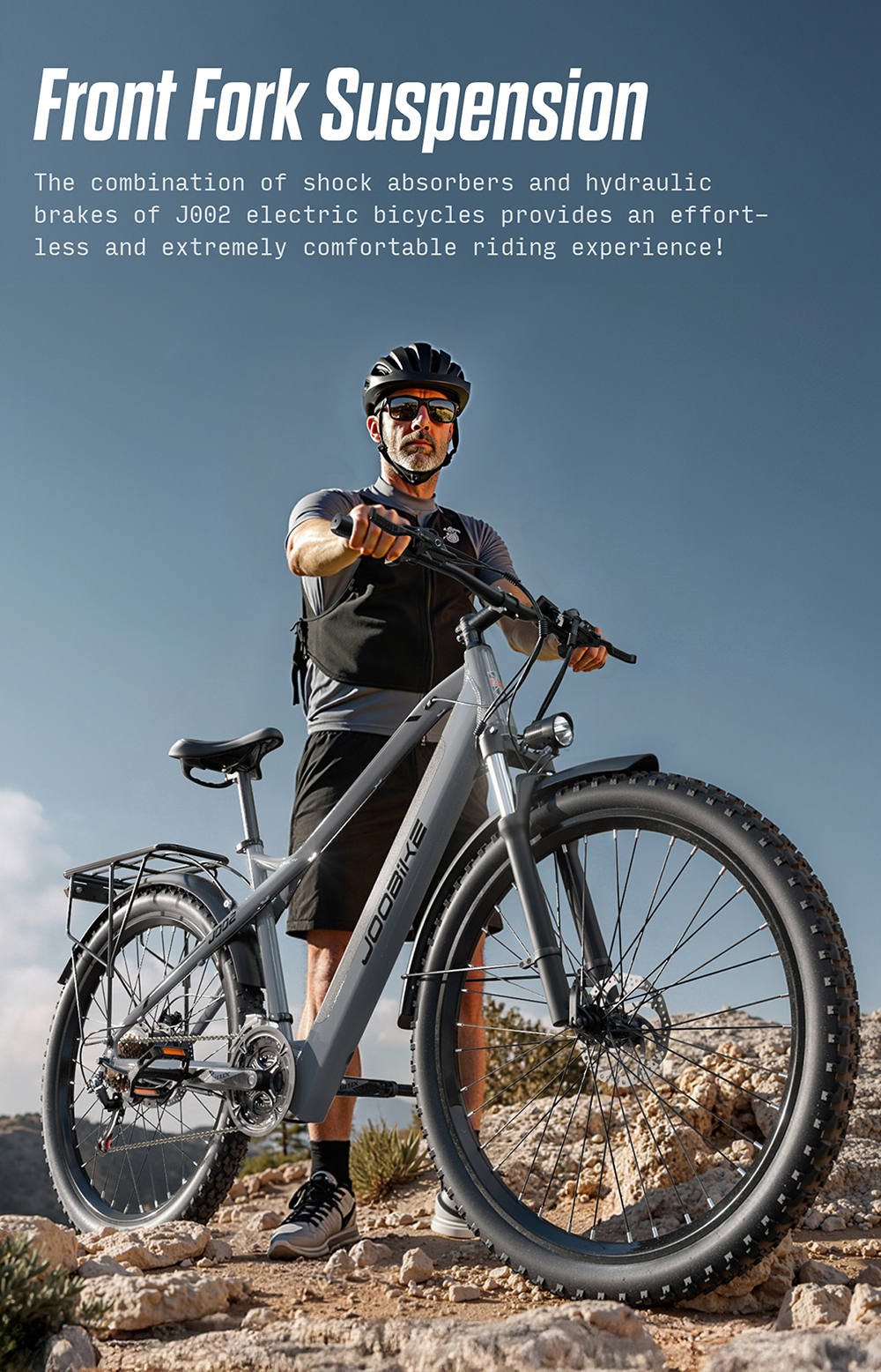 Un uomo con casco e occhiali da sole si trova su un terreno roccioso accanto a una bicicletta elettrica grigia.