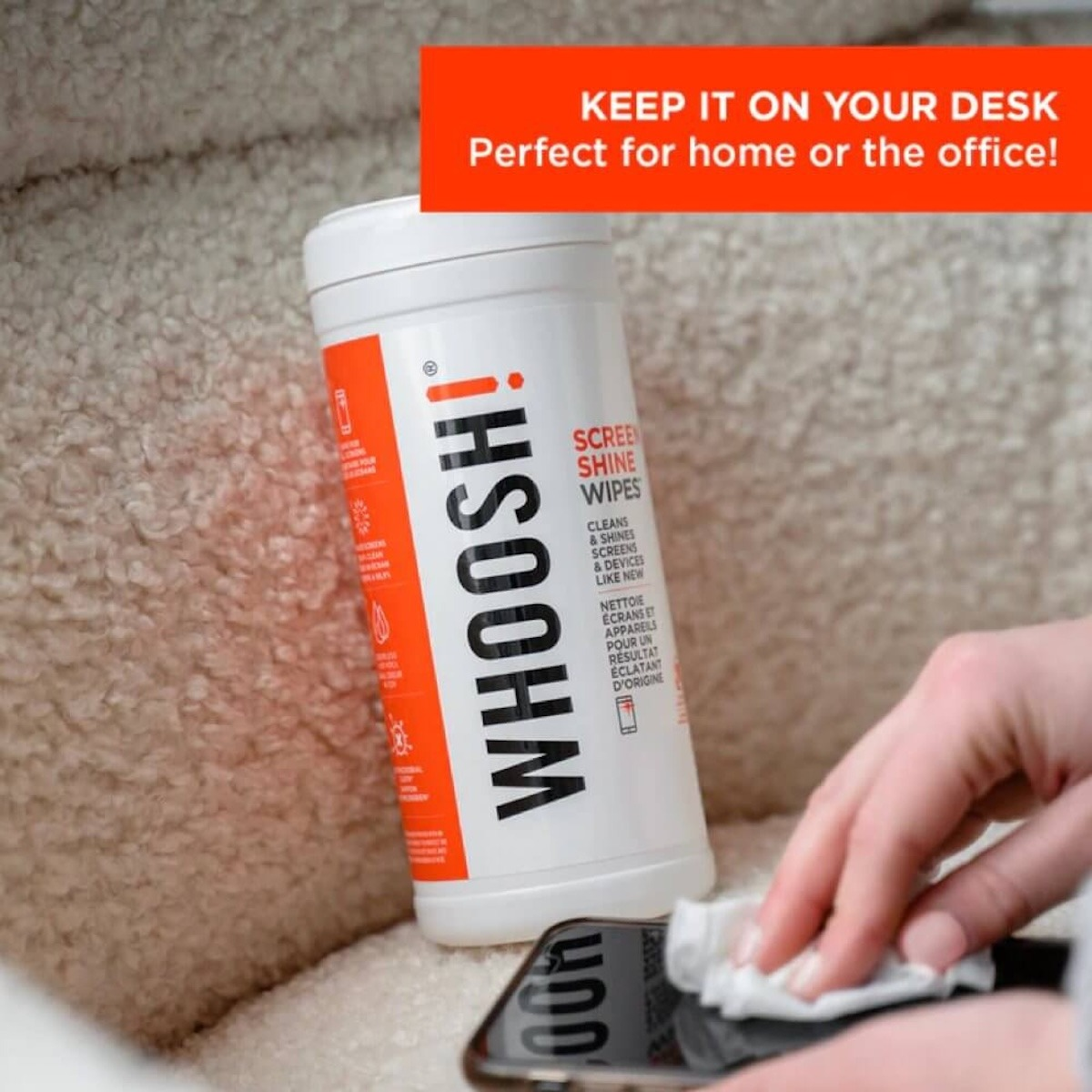 Una mano limpia un smartphone con una toallita junto a un envase de Whoosh.