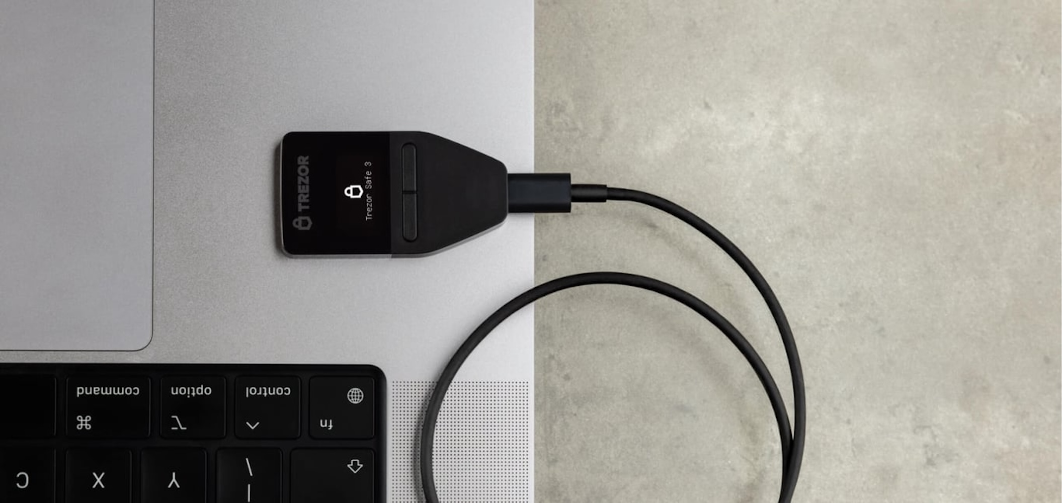 Ein schwarzes Trezor Safe 3 Krypto-Hardware-Wallet ist über ein Kabel an einen Laptop angeschlossen.