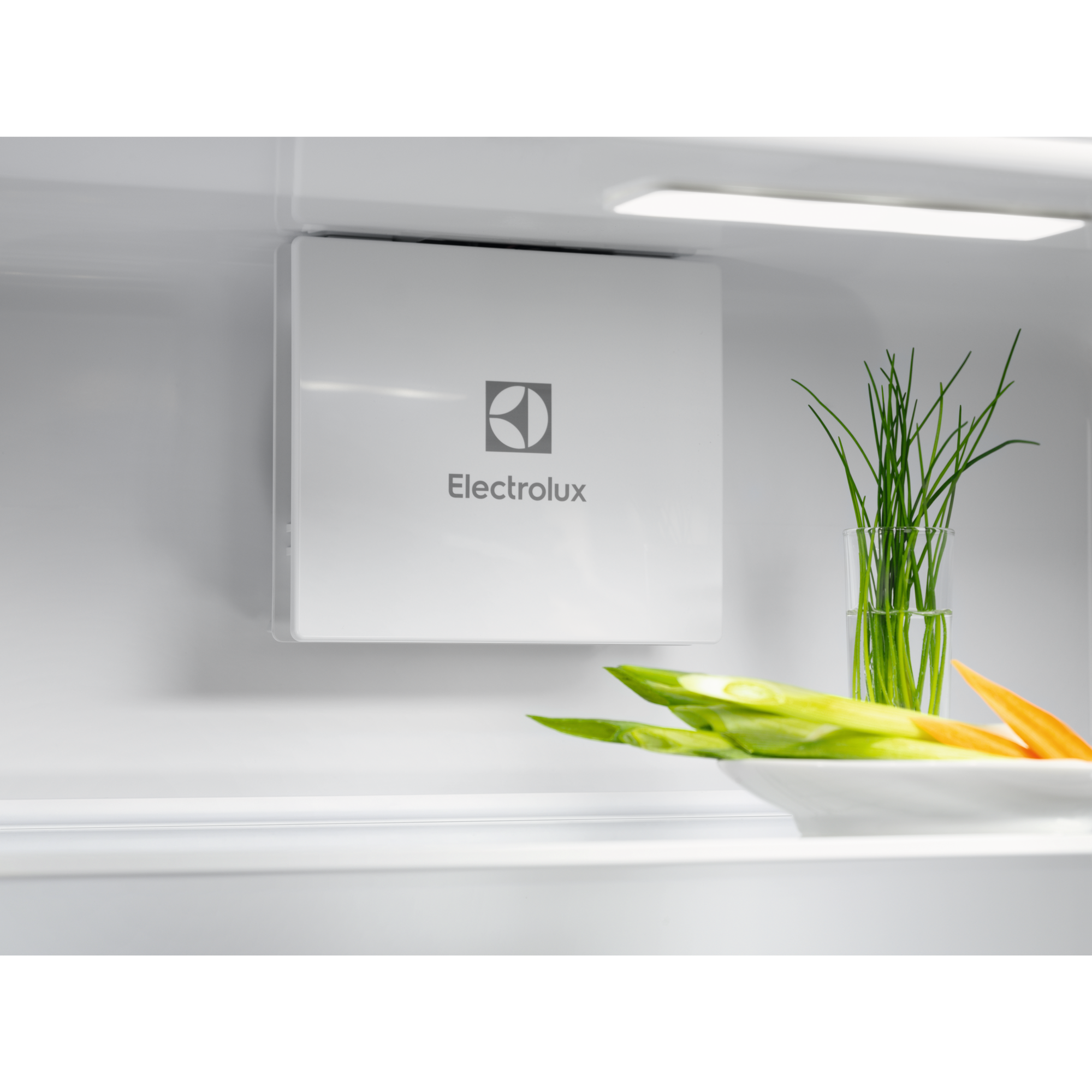 Interior de un refrigerador Electrolux con panel blanco, cebollino fresco en vaso y verduras en repisa.
