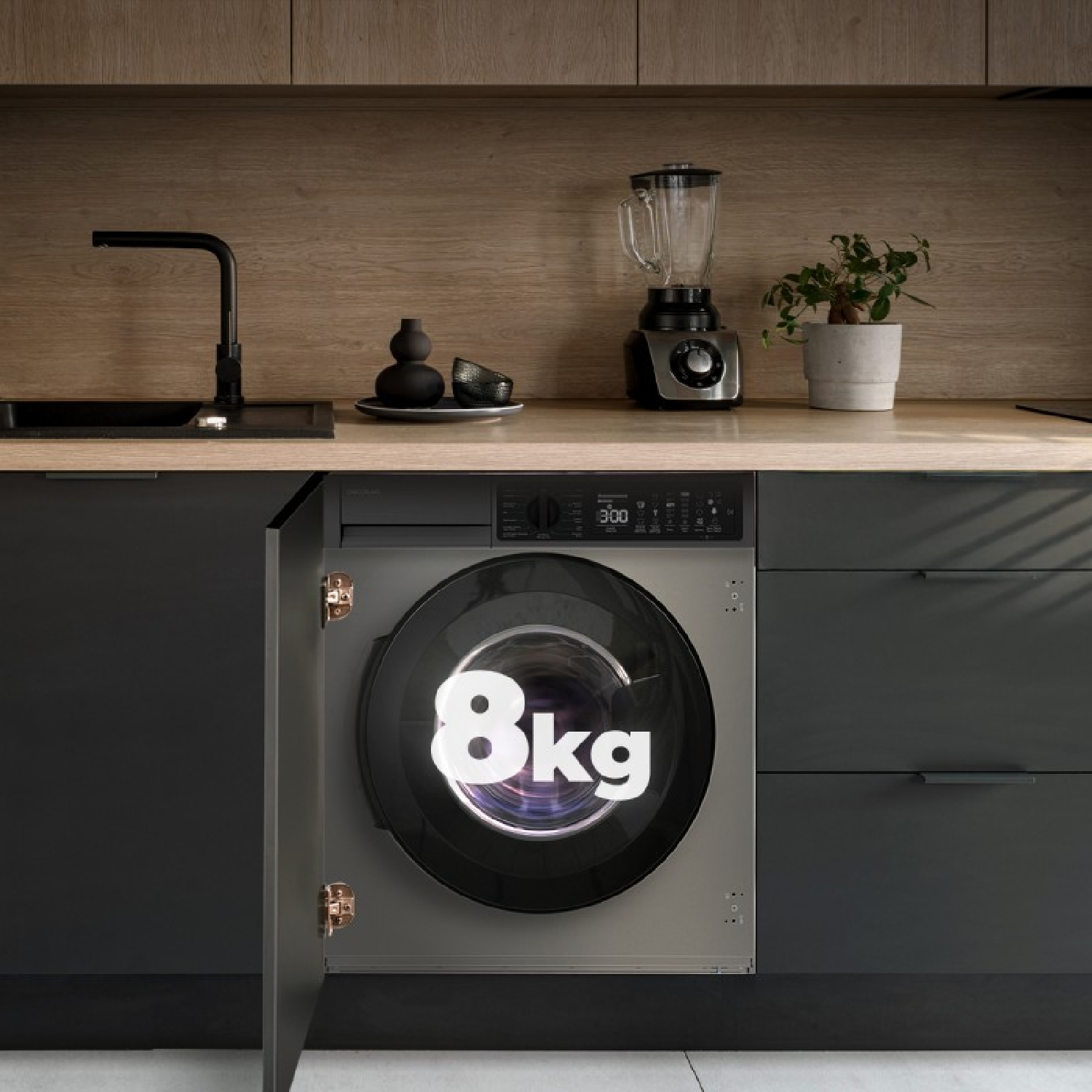 Una lavadora gris con puerta abierta y el texto '8kg' en una cocina con encimera de madera.