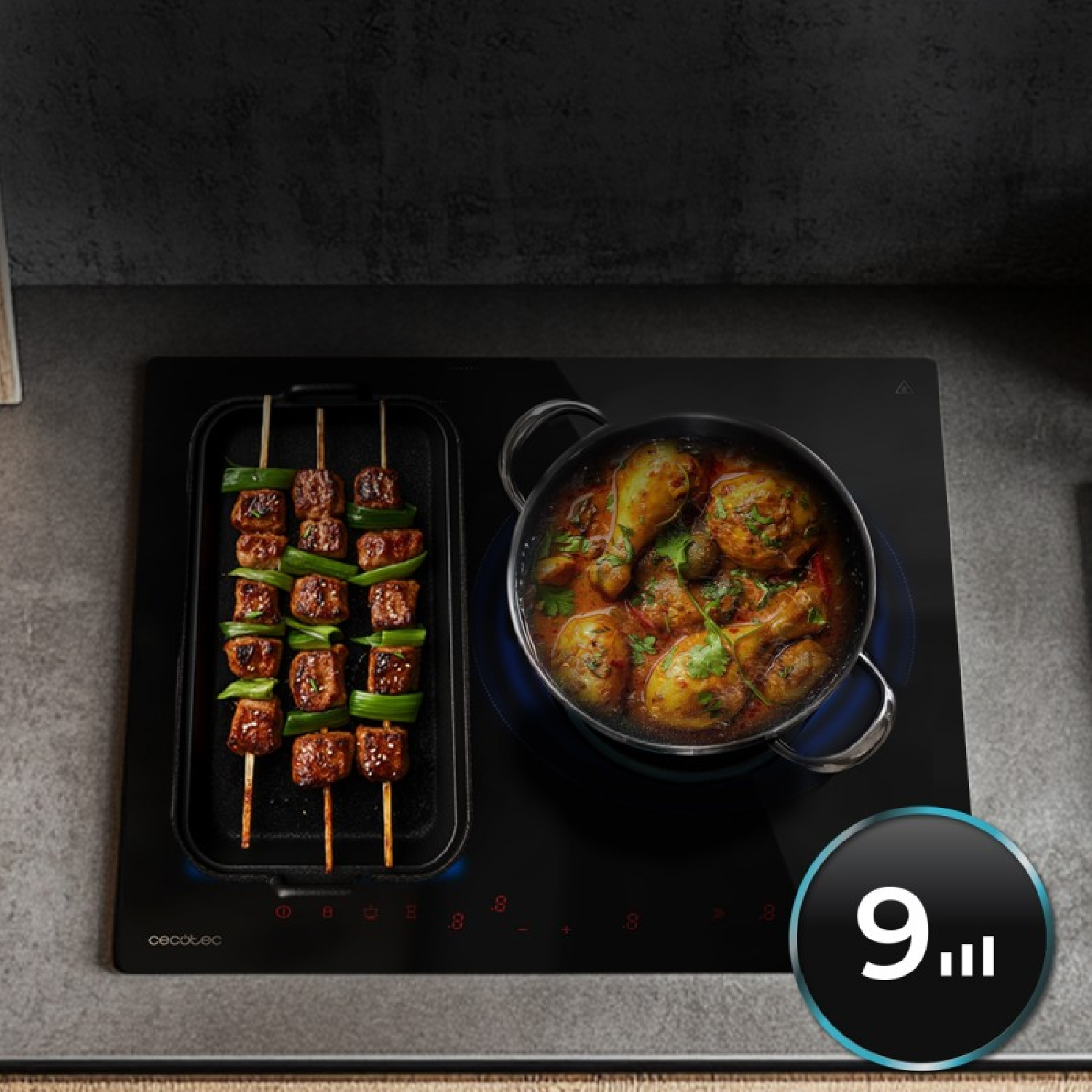 Una placa de inducción negra con brochetas en una parrilla y una olla de pollo al curry.