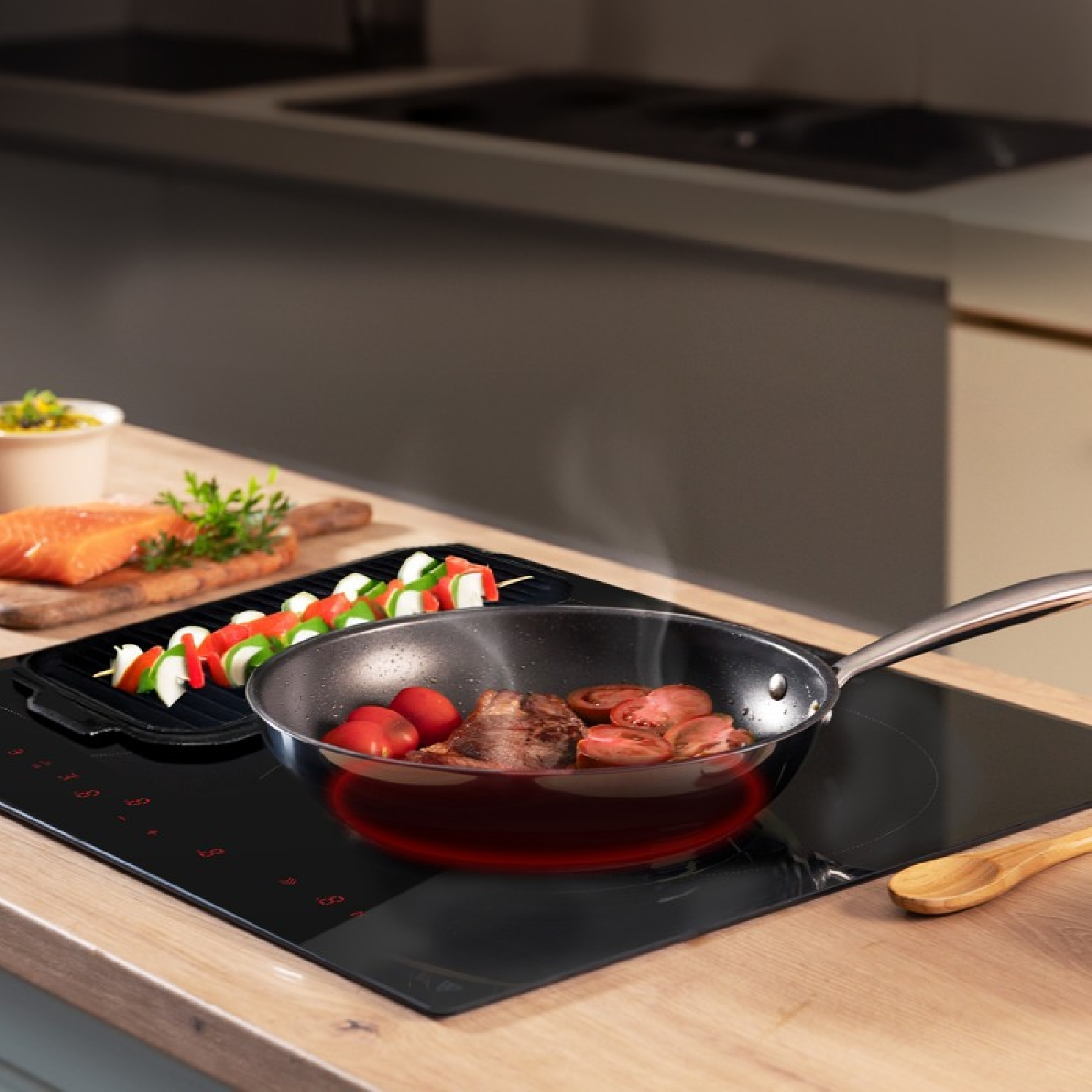 Filete y tomates se fríen en una sartén en una placa de inducción moderna con brochetas de verduras al lado.