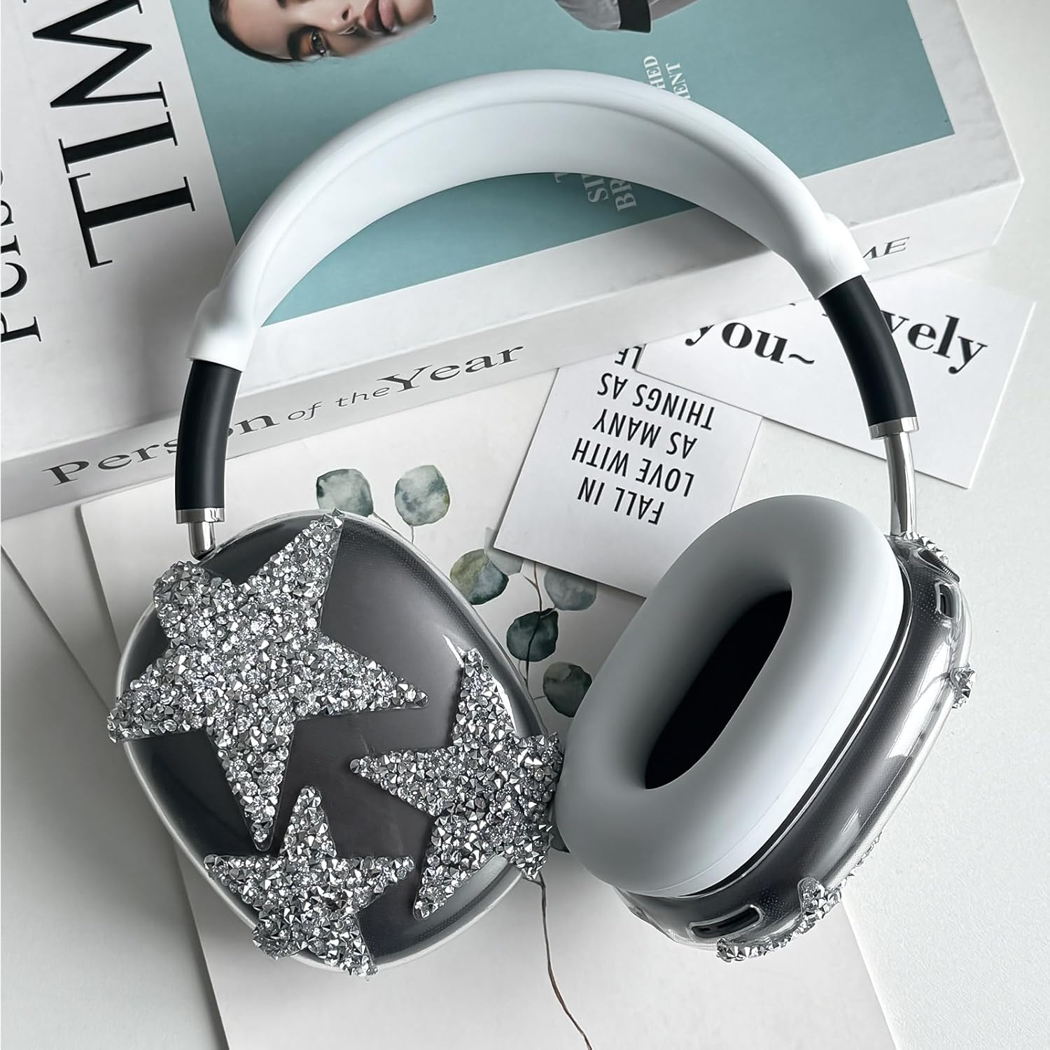 Weiße und silberne Over-Ear-Kopfhörer mit glitzernden Strass-Sternen auf Zeitschriften.