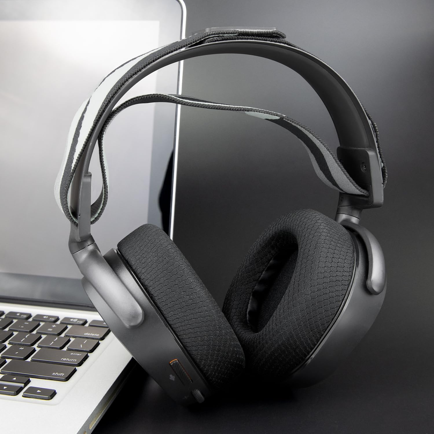 Schwarze Over-Ear-Kopfhörer mit Stoffpolstern liegen neben einem silbernen Laptop auf einem Schreibtisch.
