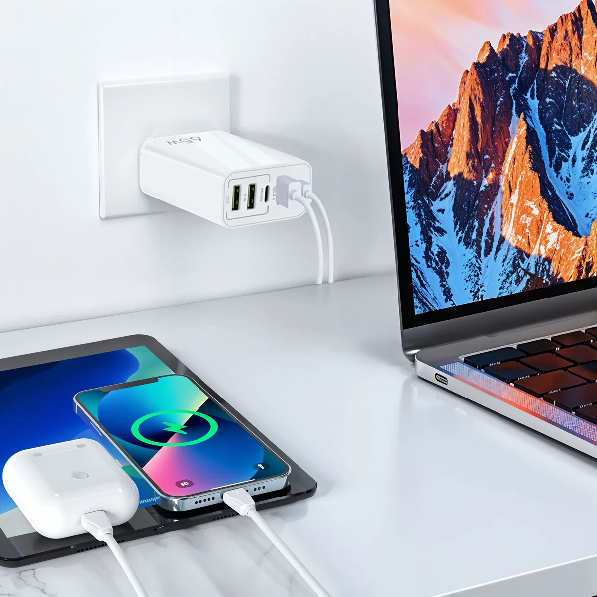 Un chargeur mural blanc de 65W alimente un ordinateur portable, une tablette et un smartphone avec des câbles sur un bureau.