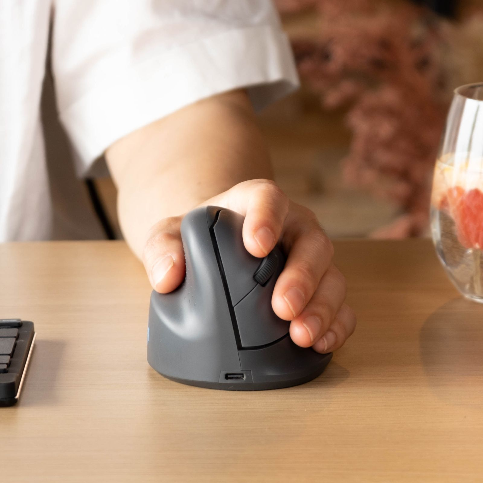 Eine Hand greift eine ergonomische, vertikale Computermaus auf einem Holztisch.
