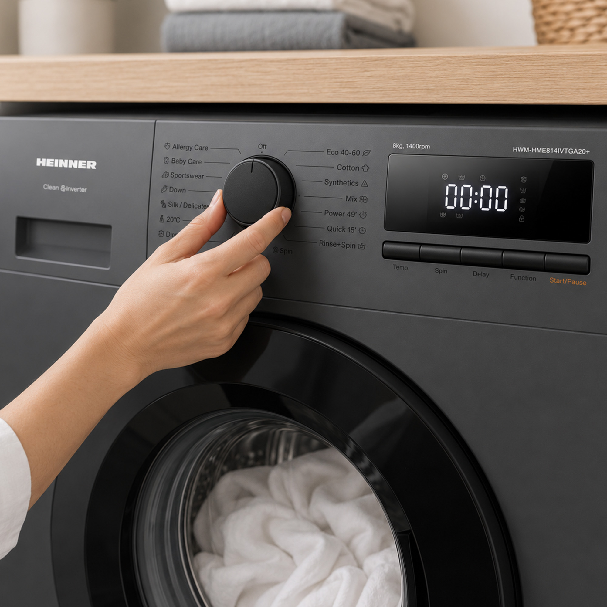 Een hand draait aan de knop van een donkergrijze Heinner wasmachine met witte was in de trommel.