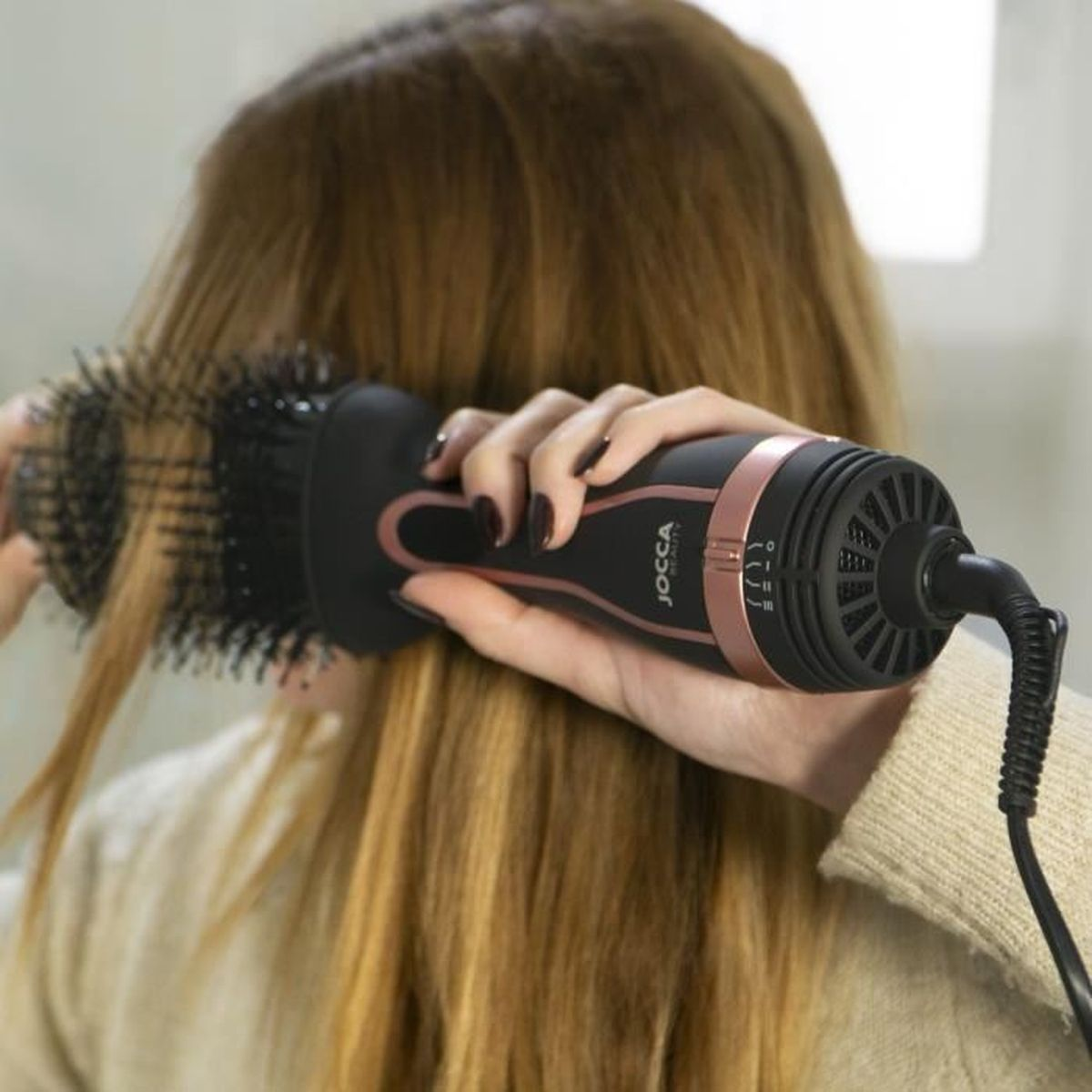 Eine Person trocknet und stylt ihr langes blondes Haar mit einer schwarz-roségoldenen Warmluftbürste.